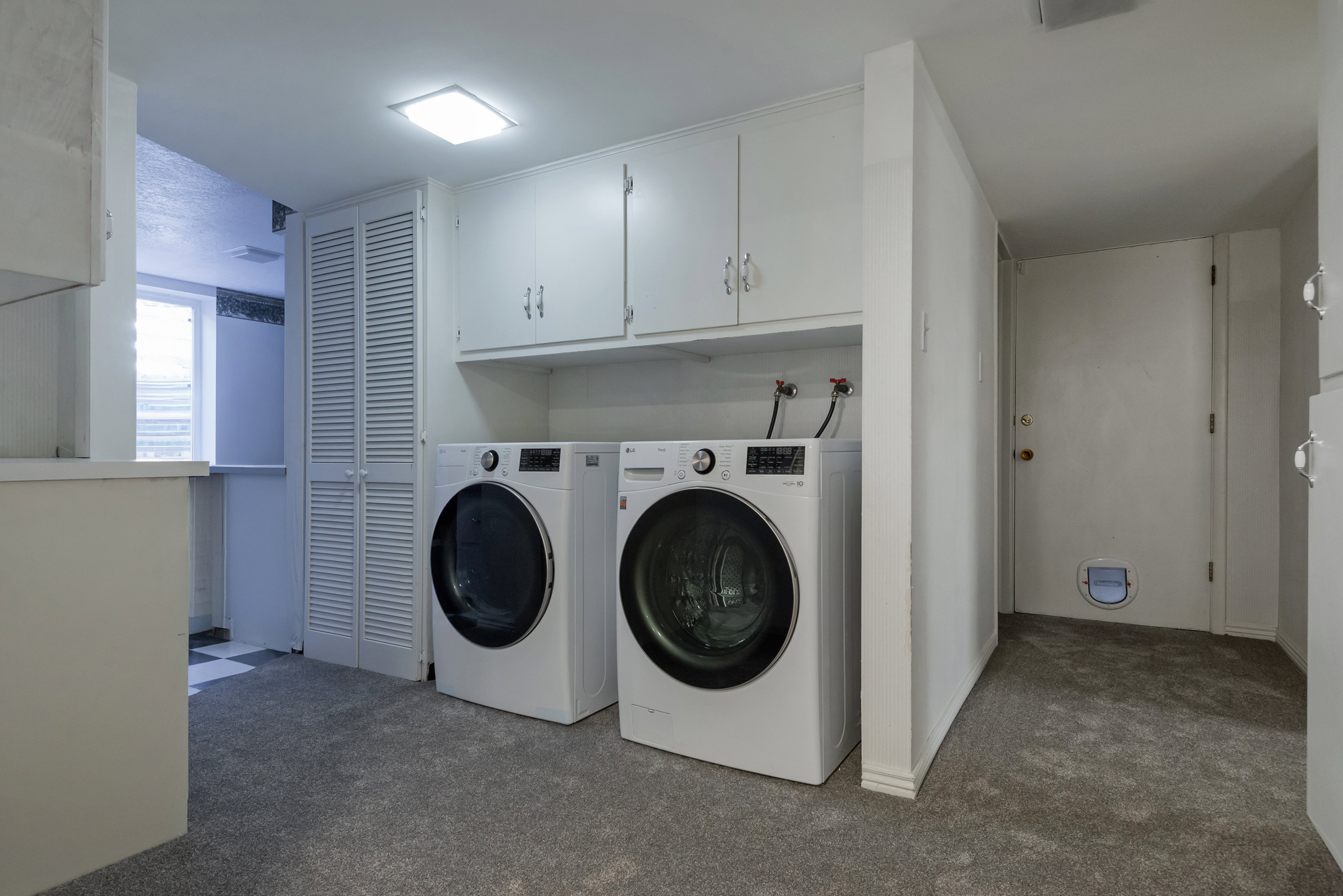 Laundry area featuring overhead cabinetry, louvered bi-fold doors, a recessed ceiling light, and gray carpeting