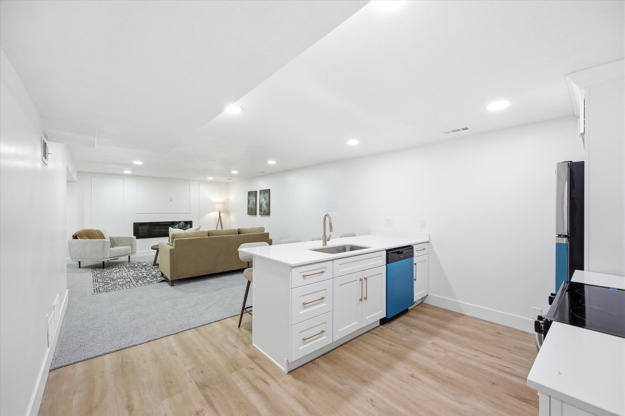 Kitchenette with white shaker cabinetry, stainless steel sink with gooseneck faucet, quartz countertops, and wood-finish flooring