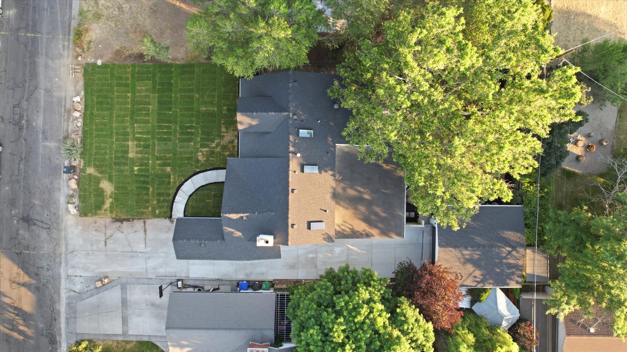 Aerial perspective showcasing a property with a newly installed sod lawn, a curved concrete pathway, mature trees, and a dark shingle roof