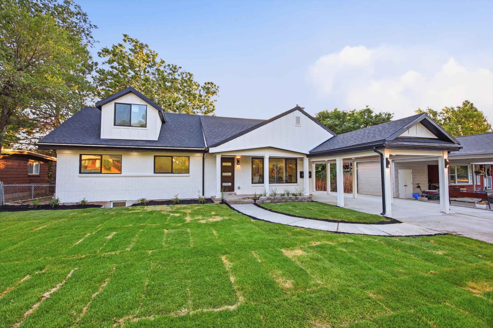 Contemporary residence featuring a white brick and vertical siding exterior, a dark shingle roof, a covered entry, a covered carport, and a dormer window