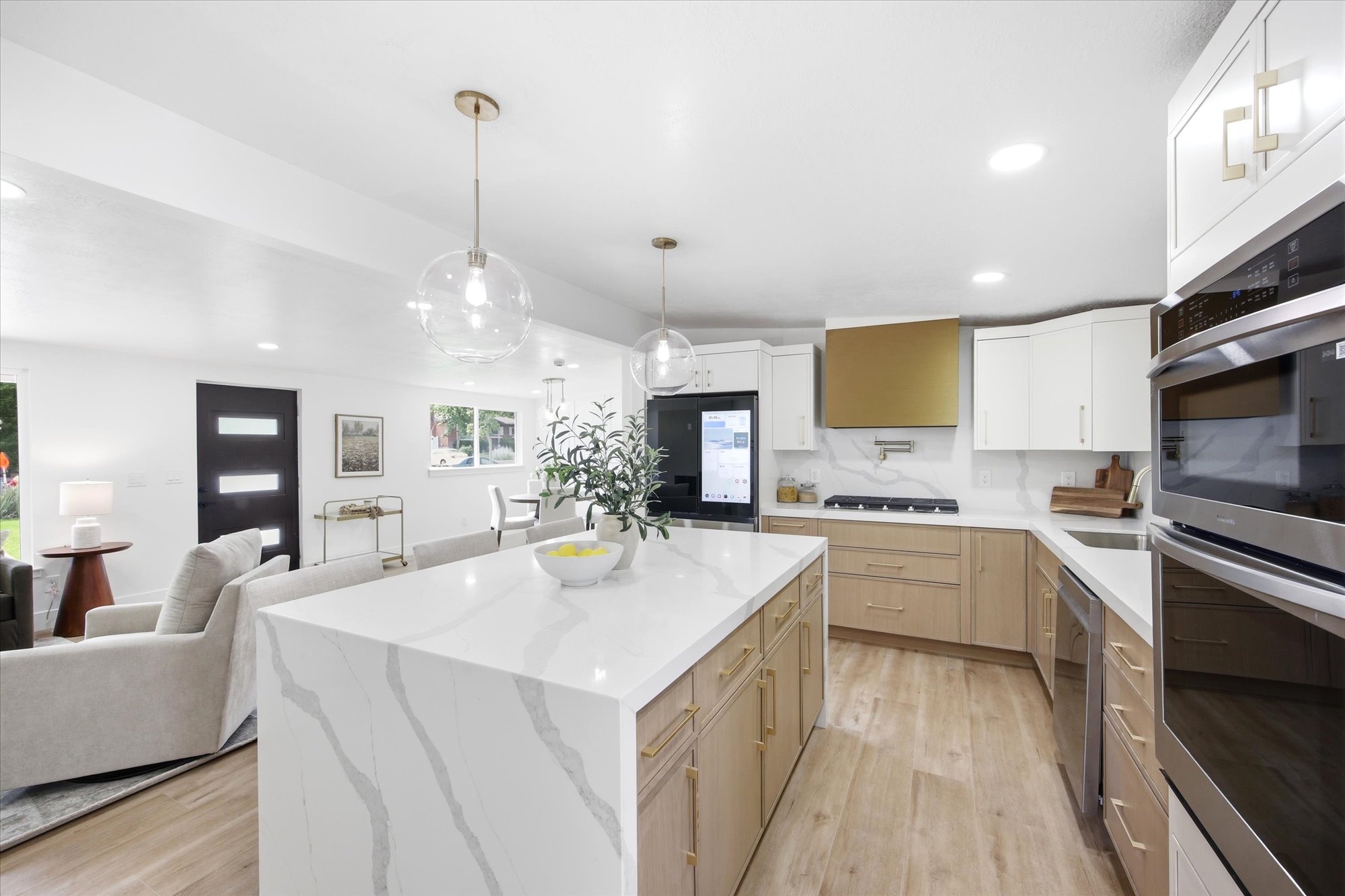 Contemporary kitchen featuring a waterfall island with a stone countertop, gold-tone hardware throughout, integrated stainless steel appliances, a gold-tone range hood, and wood-finish flooring