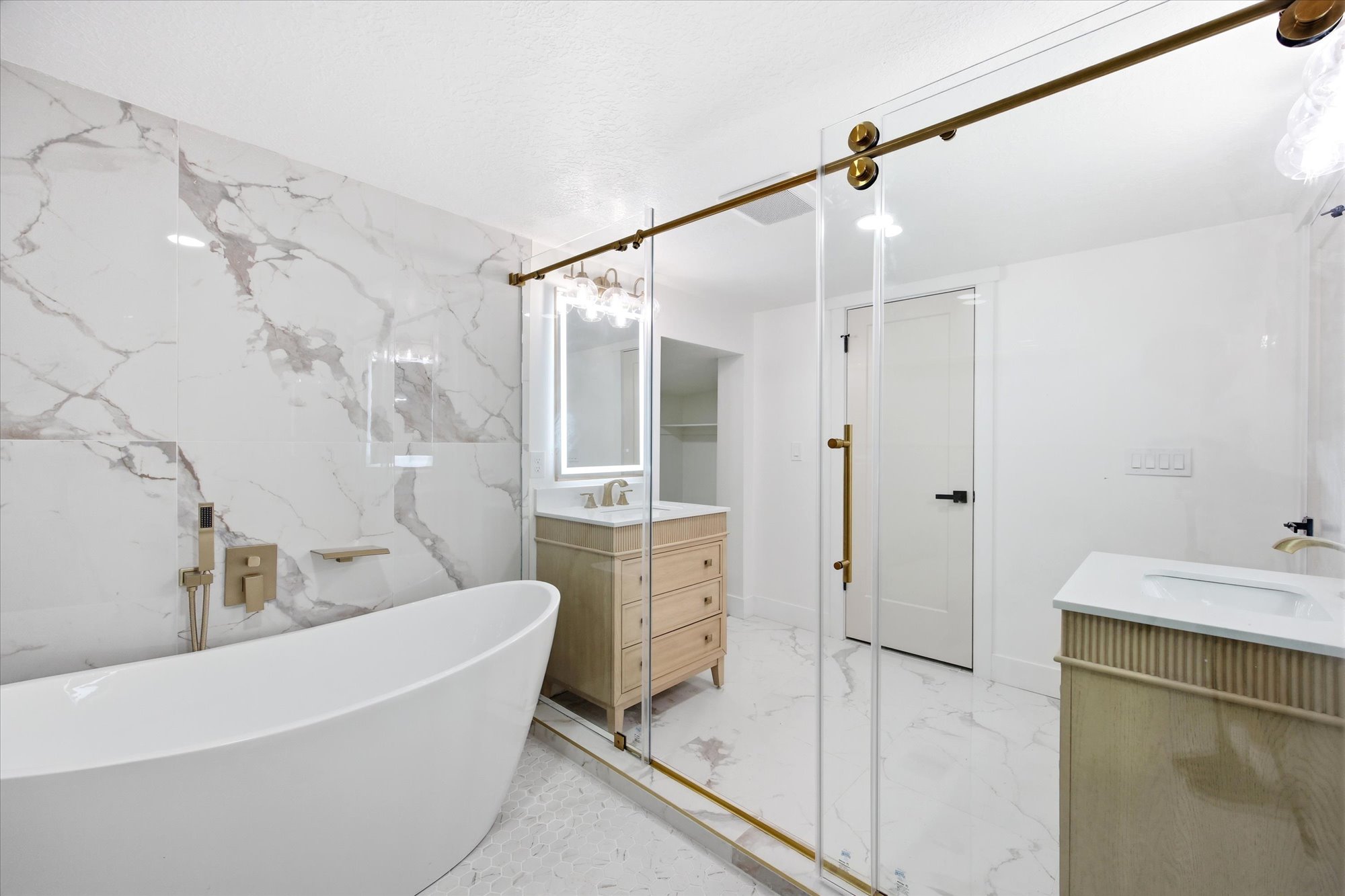 Freestanding soaking tub with brushed brass fixtures and marble-look tiled accent wall