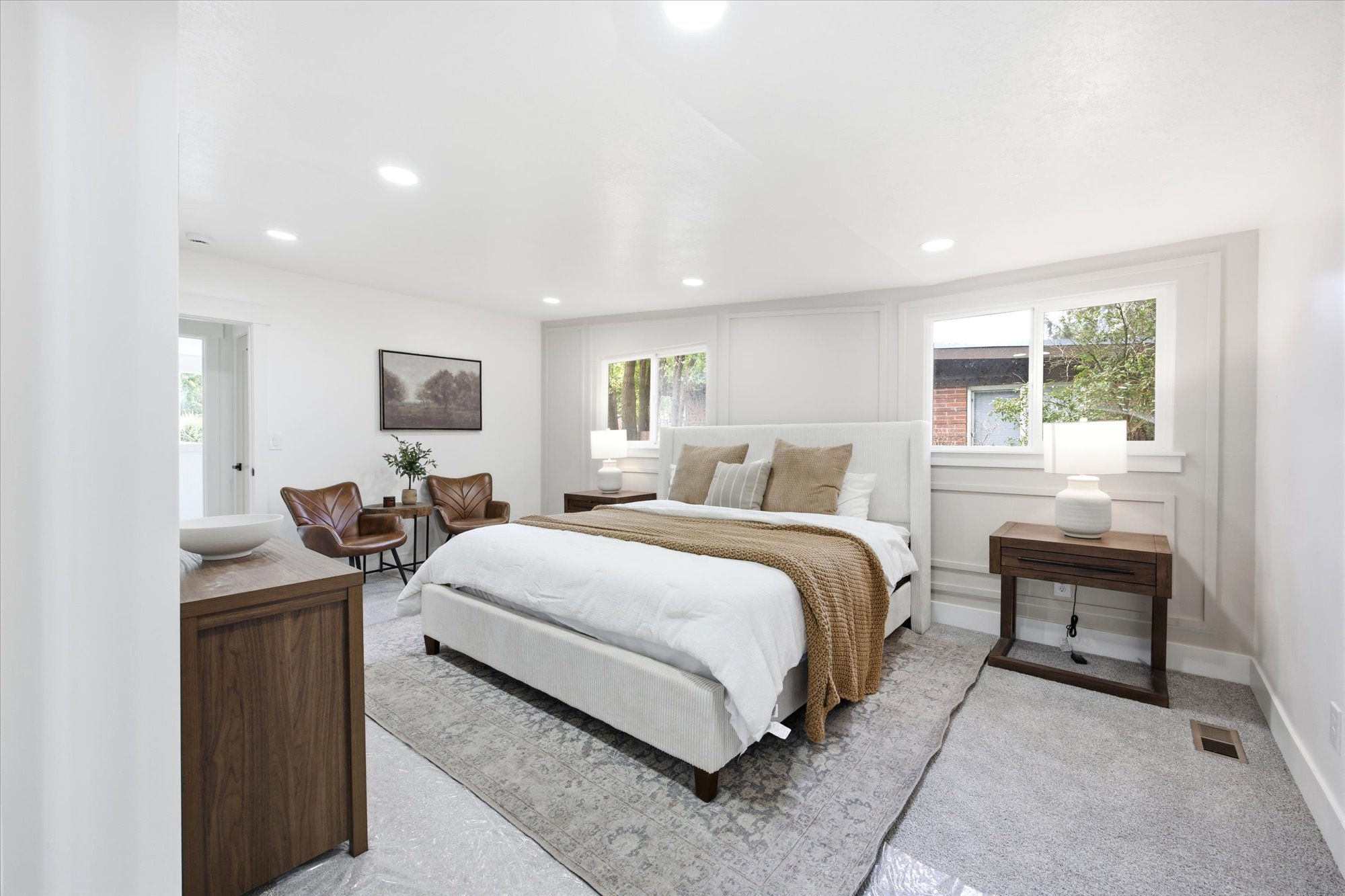 Bright bedroom featuring recessed lighting, a paneled accent wall, two windows, and a glass-paneled door