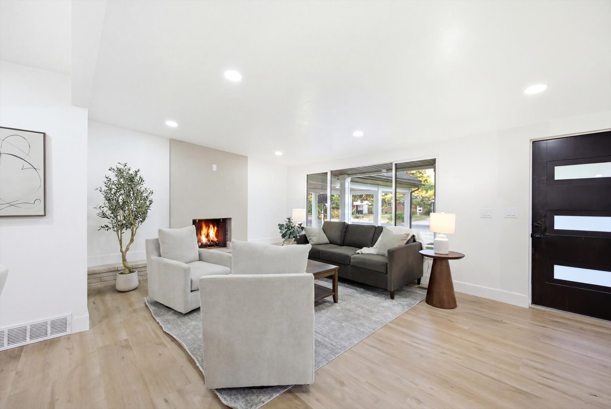 Spacious living area featuring wood-finish flooring, a modern fireplace with a light-toned surround, large picture windows, and recessed lighting