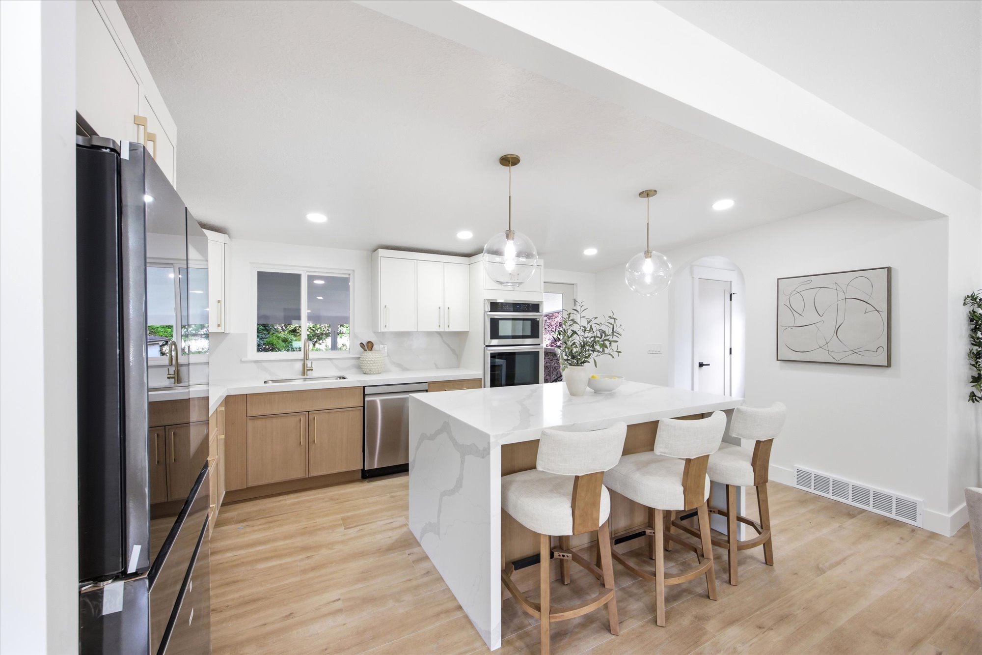 Kitchen featuring a large waterfall island with seating, pendant lighting, stainless steel appliances, wood-finish flooring, and two-tone cabinetry