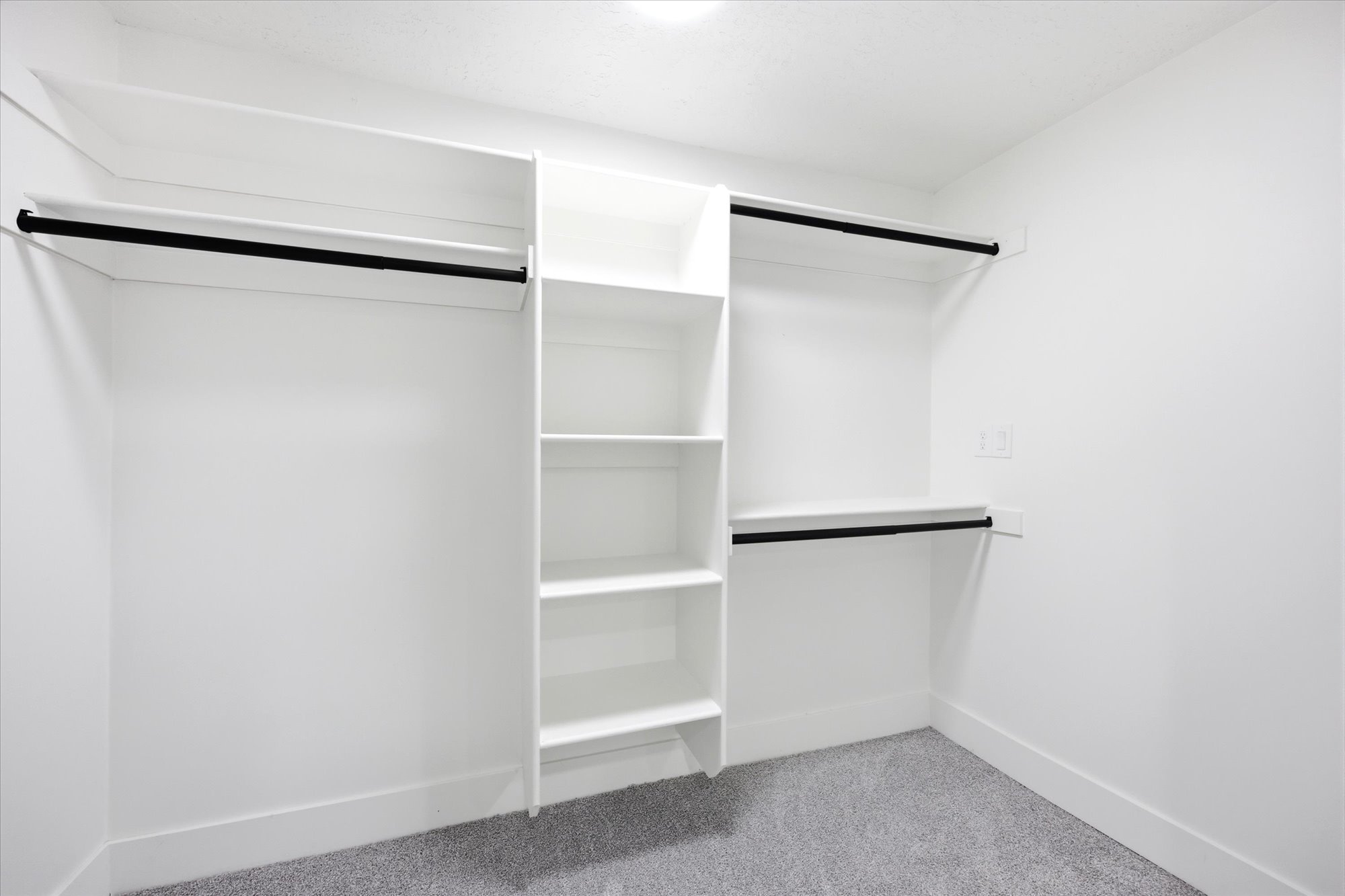 Spacious closet with white shelving, multiple hanging rods, and light gray carpeting