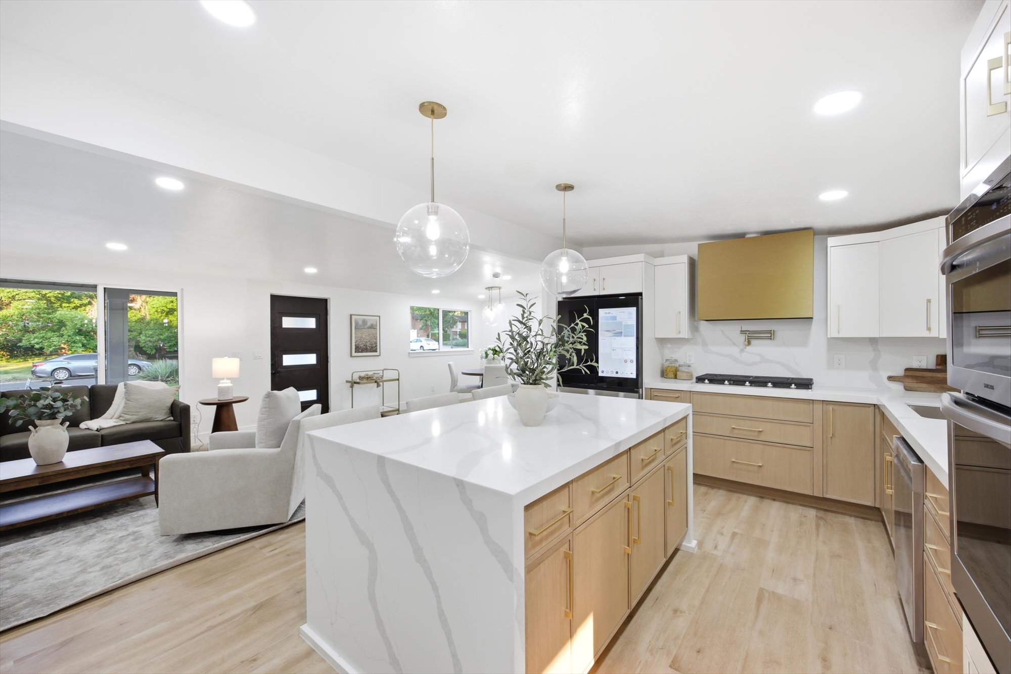 Open-concept kitchen and living area featuring a waterfall island with a quartz countertop, gold-toned hardware, recessed lighting, and wood-finish flooring
