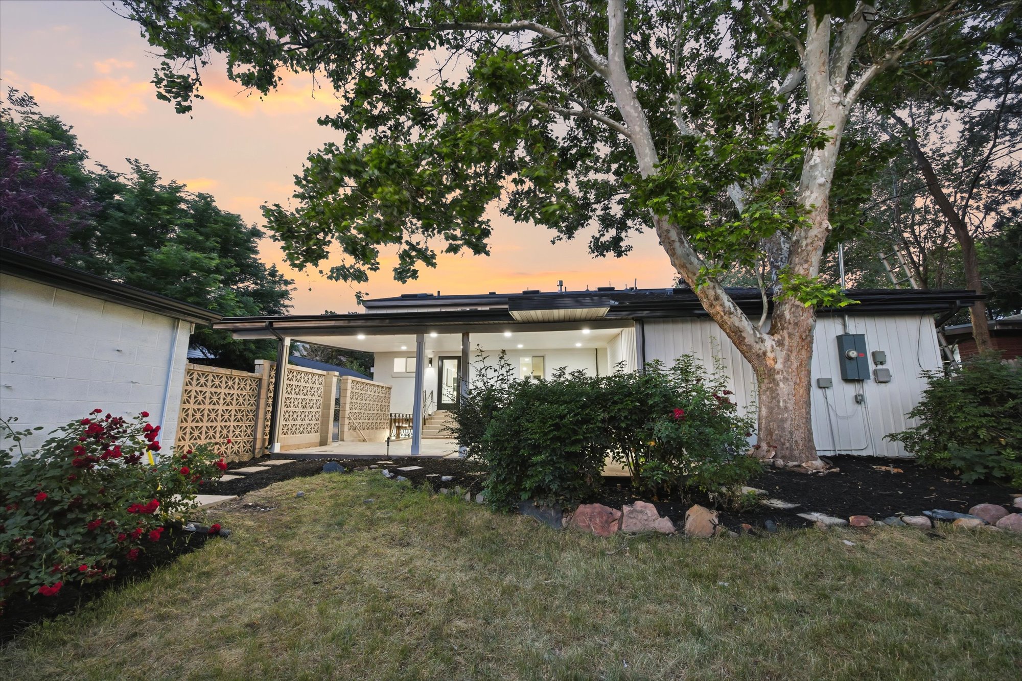 Expansive backyard with a covered patio, a stone pathway, mature trees, and a decorative block wall