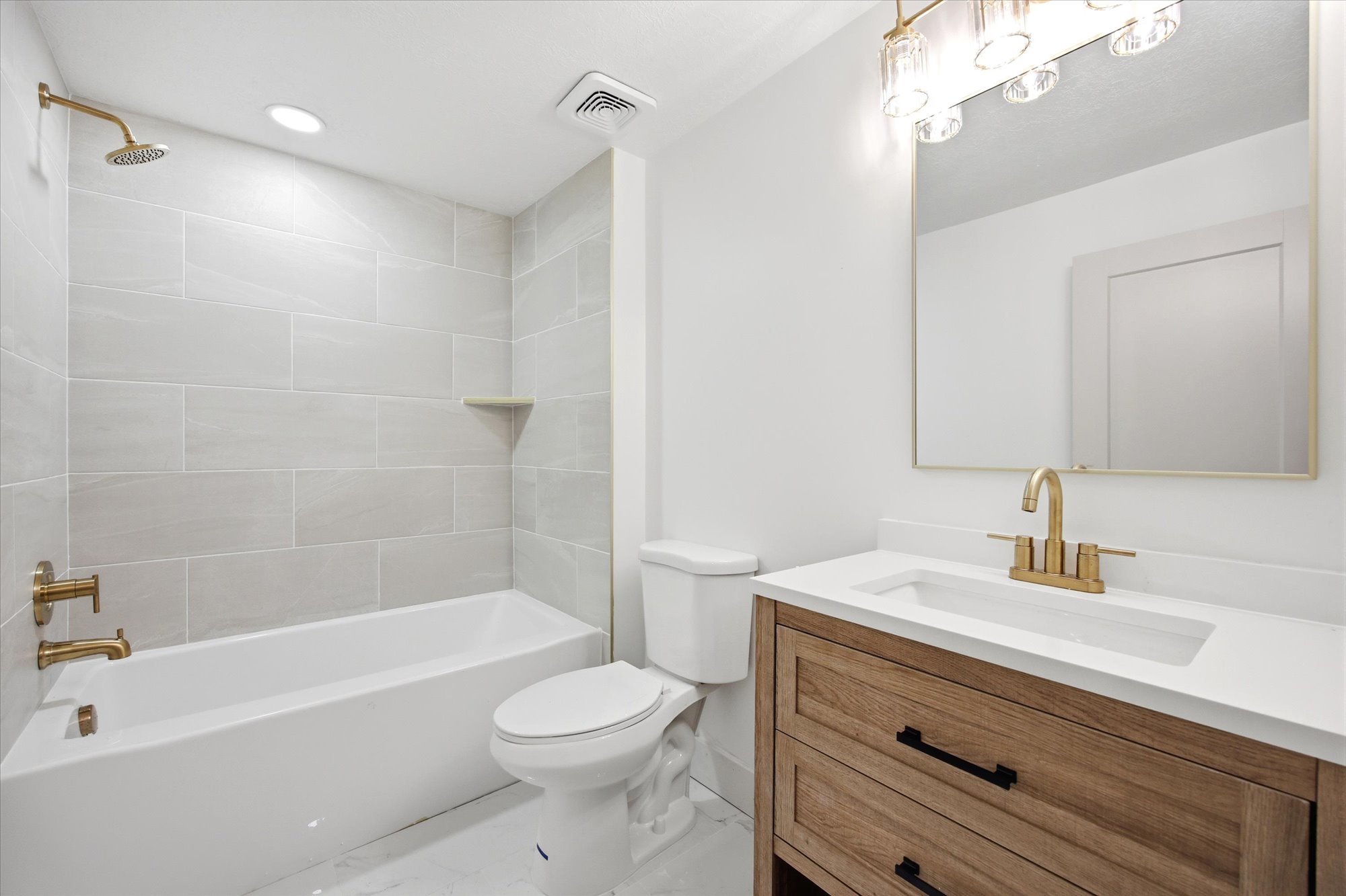 Contemporary bathroom featuring a white soaking tub with brass fixtures, a matching brass rain shower head, and light-toned rectangular wall tiling