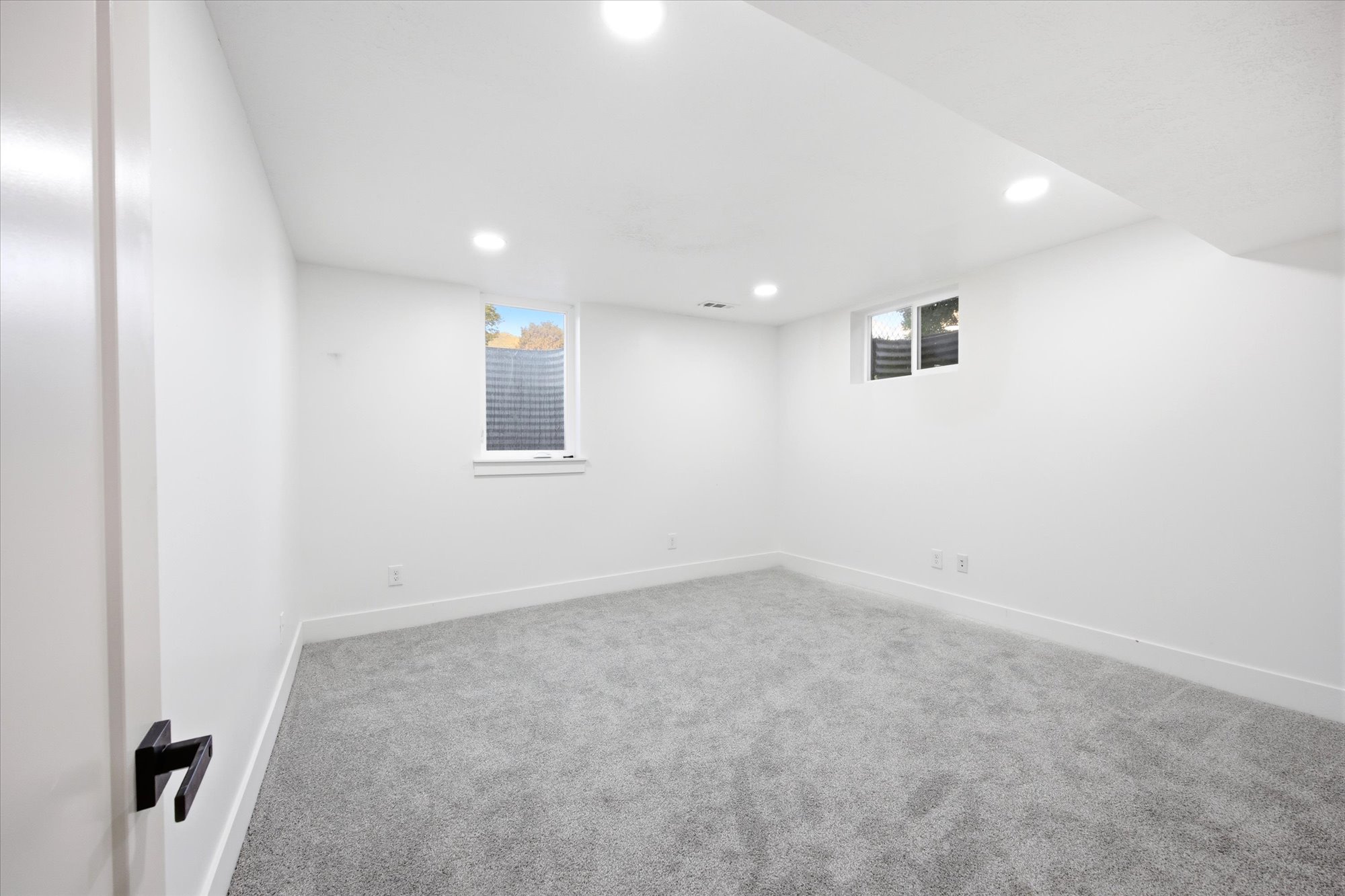 Bright room featuring light gray carpet, white walls, recessed lighting, and two windows