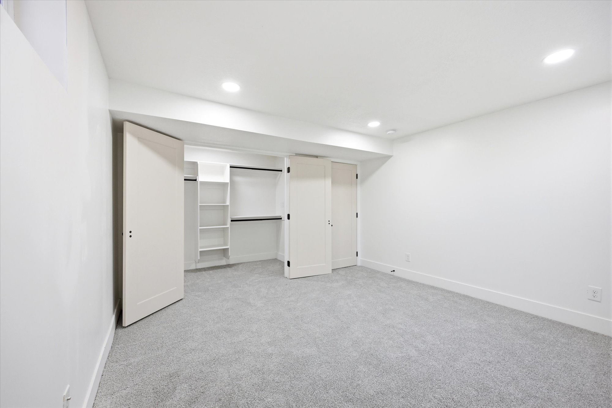 Bedroom featuring light gray carpeting, white walls, recessed ceiling lighting, and a closet with bifold doors and built-in shelving