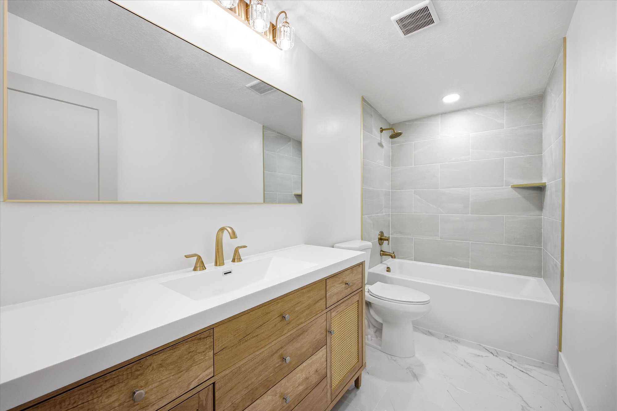 Bathroom featuring a wood-finish vanity with an integrated white sink, gold-tone hardware, and a large mirror