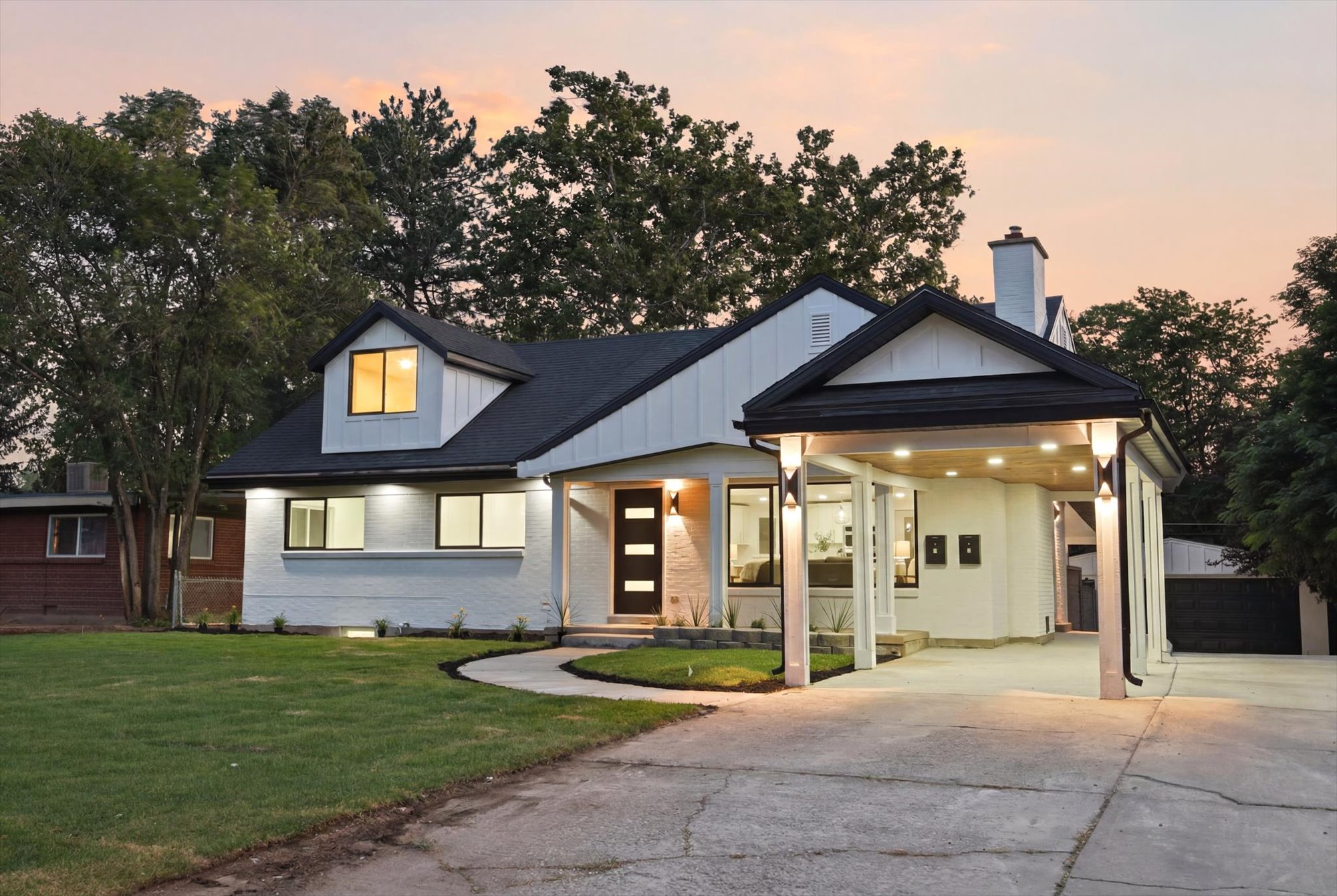 Modern farmhouse exterior featuring white painted brick, black trim, a gabled roofline, and a prominent covered carport with recessed lighting