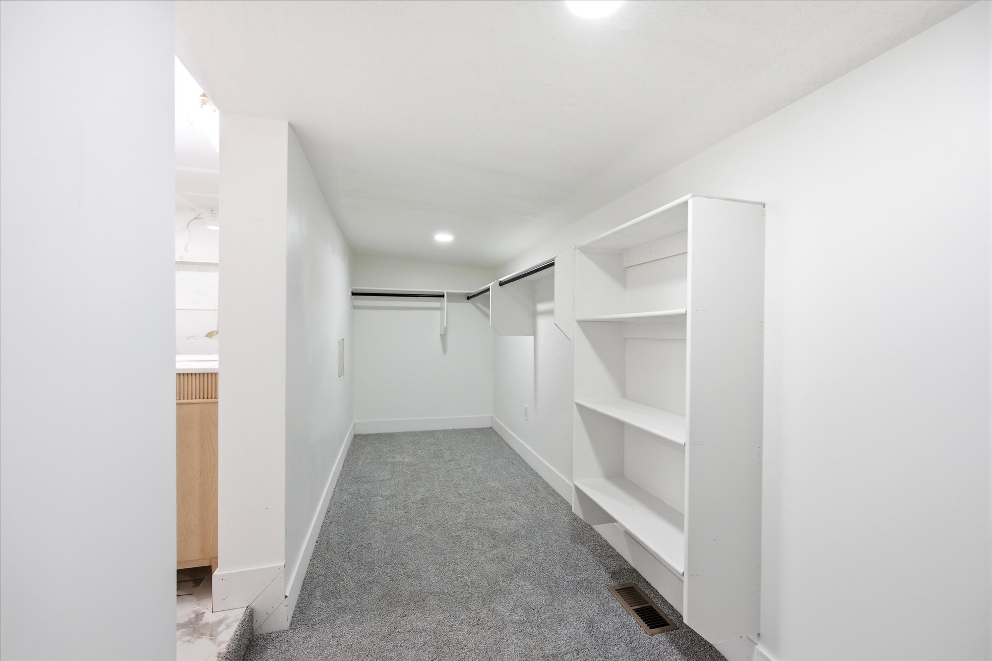 Spacious walk-in closet featuring built-in shelving, hanging rods, recessed lighting, and gray carpeting