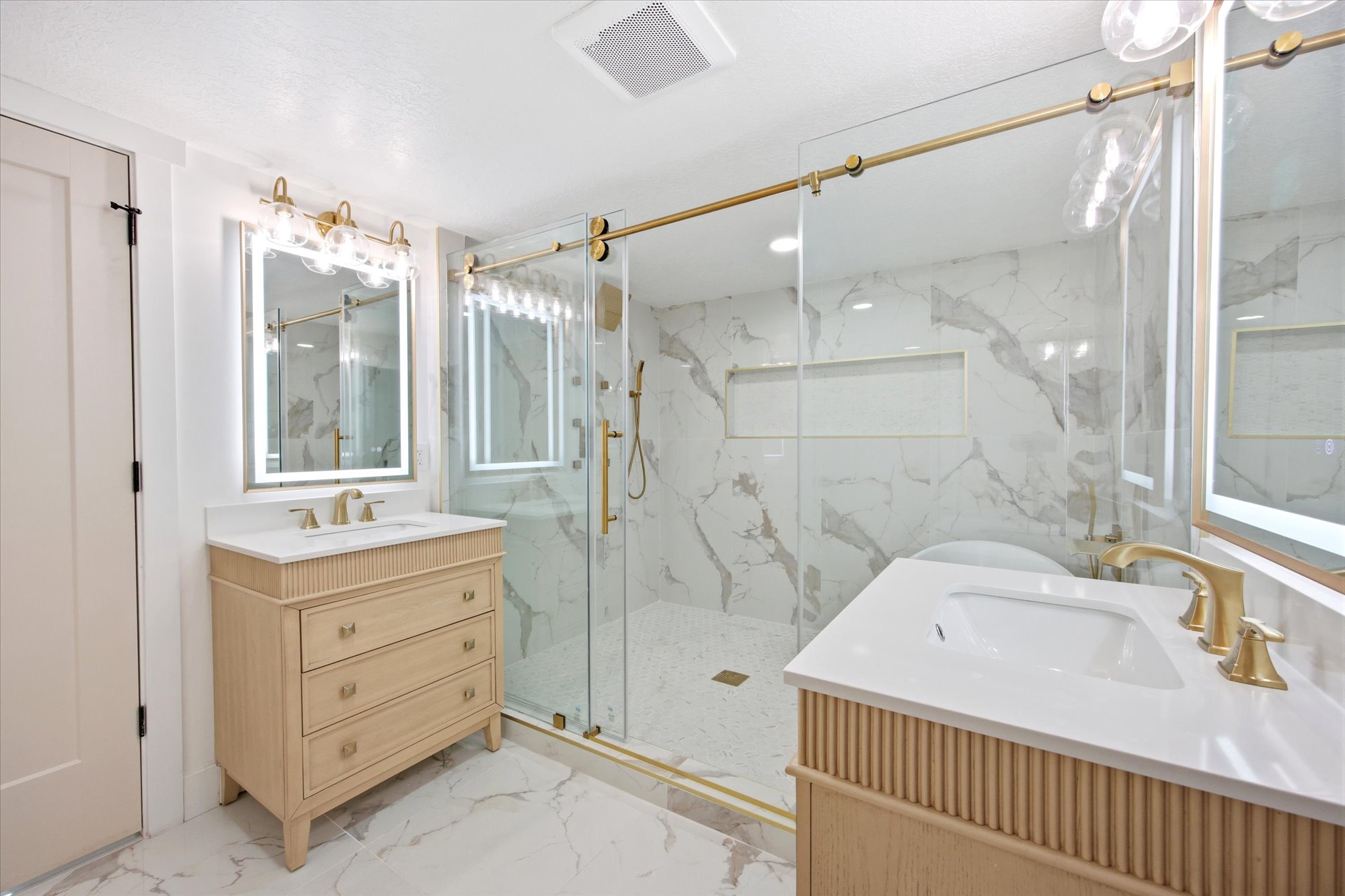 Dual vanity bathroom featuring light wood-finish cabinetry, white countertops, and gold-finish hardware