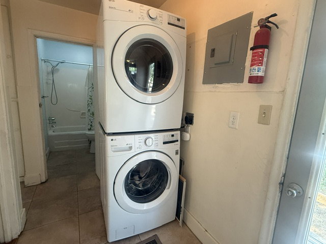 Laundry area with stacked washer and dryer, tile flooring, and a nearby full bathroom featuring a tub with shower