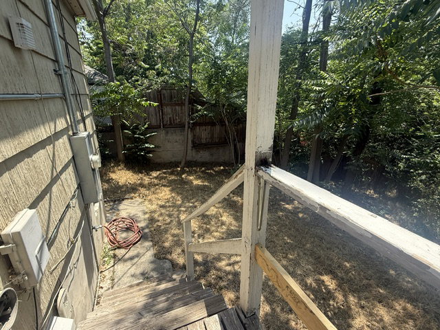 Backyard space featuring mature trees, a concrete walkway, and a wooden fence