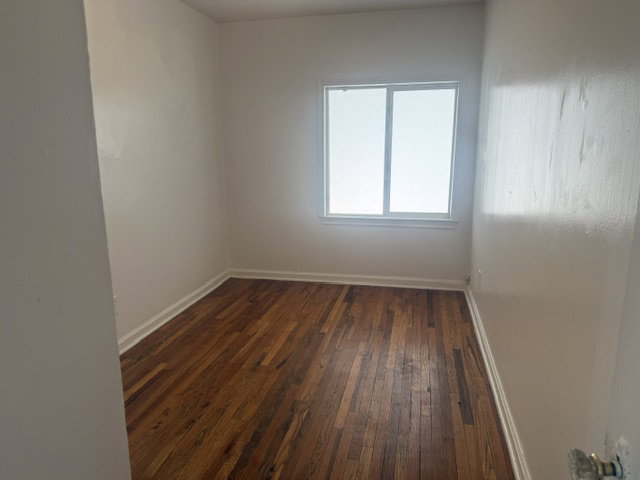 Room featuring wood-finish flooring, white baseboards, and a white window frame