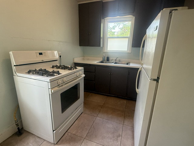 Kitchen featuring a white gas range, a white refrigerator, brown cabinetry, and a white sink with a window overhead