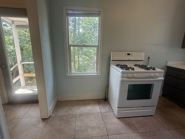 Kitchen area featuring a white freestanding gas range, tile flooring, light blue wall paint, a window, and an exterior door leading to a wooden deck