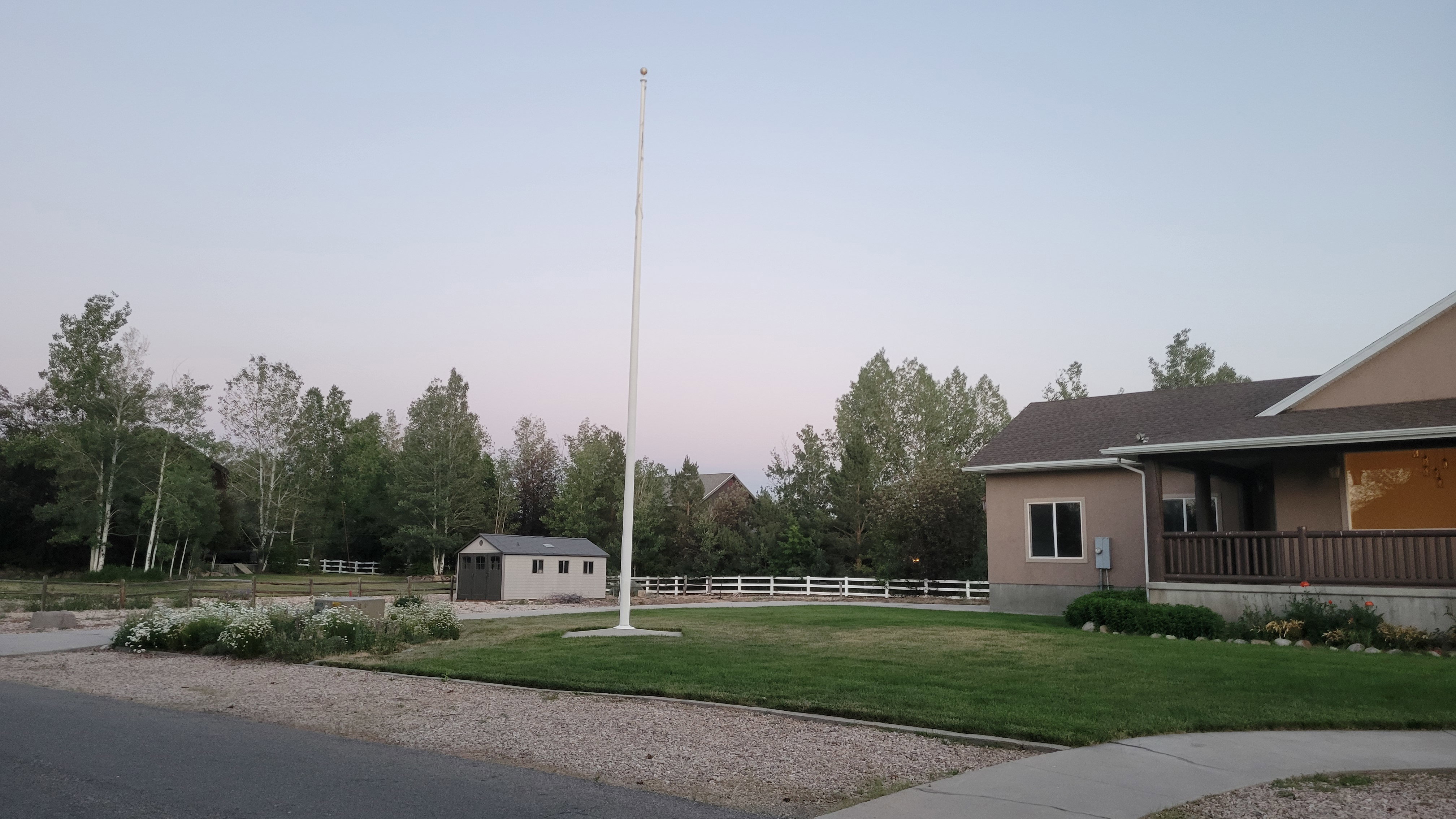 Expansive front yard featuring a manicured lawn, gravel driveway, and mature landscaping