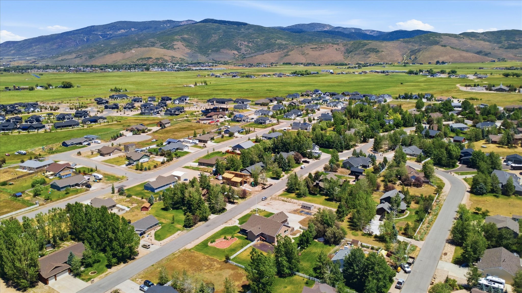 Aerial overview of a residential neighborhood with diverse architectural styles, mature trees, paved streets, and a mountainous backdrop