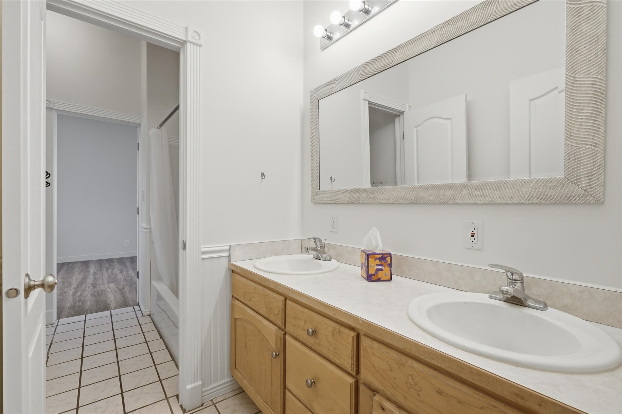 Bathroom featuring a dual-sink vanity with wood cabinetry, a large framed mirror, and a tile floor