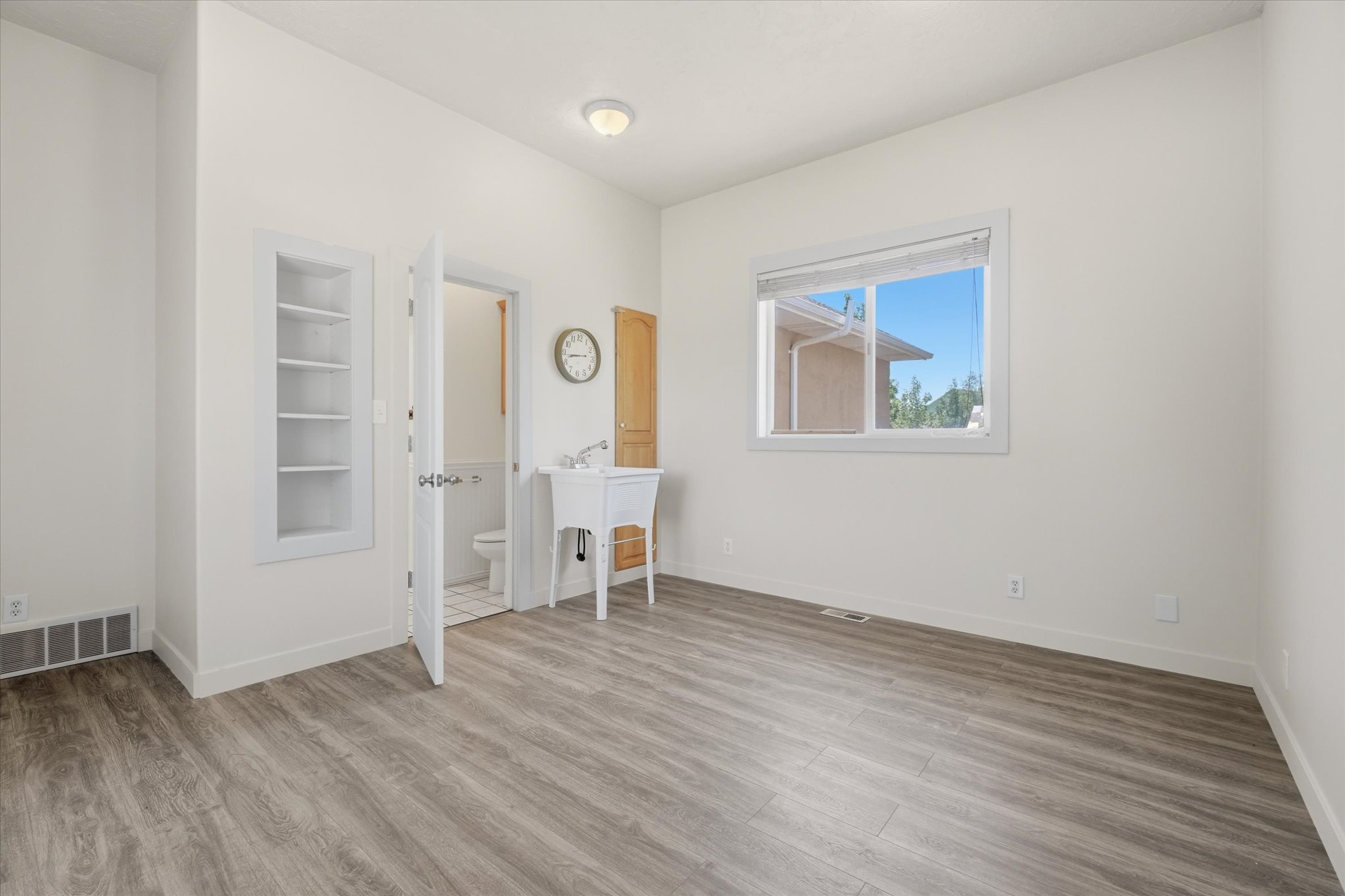 Spacious room featuring wood-finish flooring, a built-in shelving unit, and a window with natural light