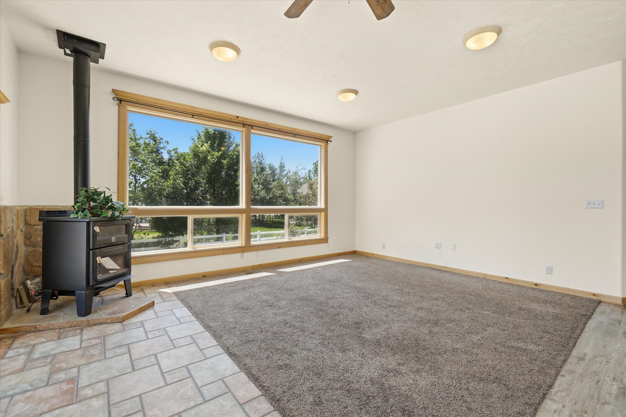 Spacious room featuring a wood-burning stove with a stone surround, large windows, ceiling fans, recessed lighting, and mixed flooring with carpet and tile