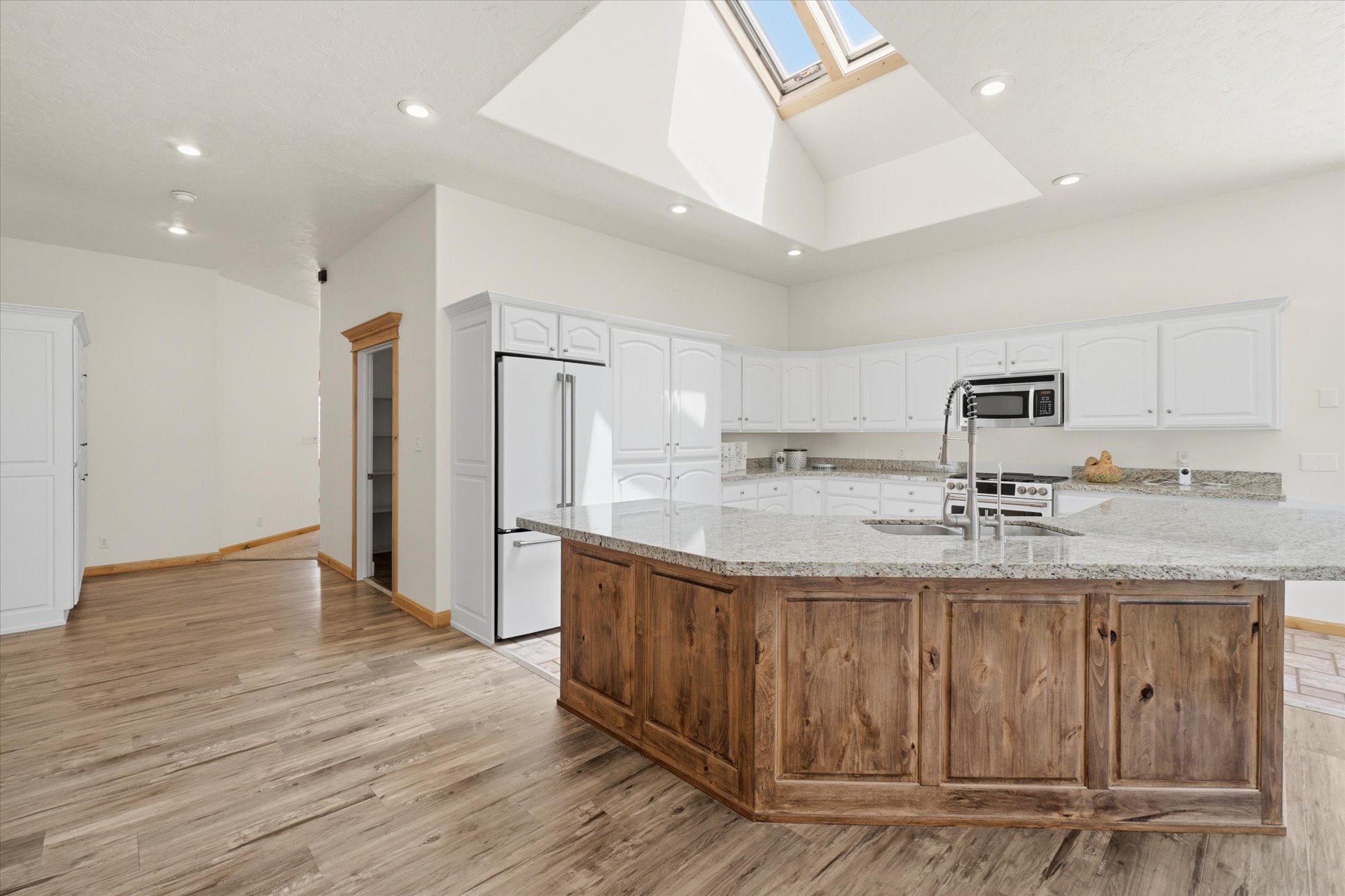 Spacious kitchen featuring a large central island with wood-finish cabinetry, light-toned countertops, and an undermount sink with a gooseneck faucet