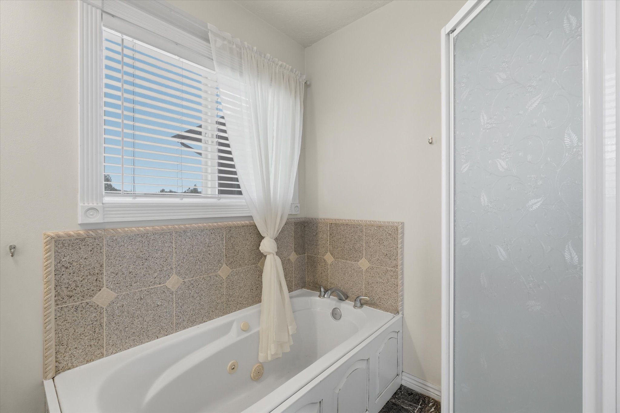 Jetted soaking tub with decorative tile surround and an adjacent glass-enclosed shower