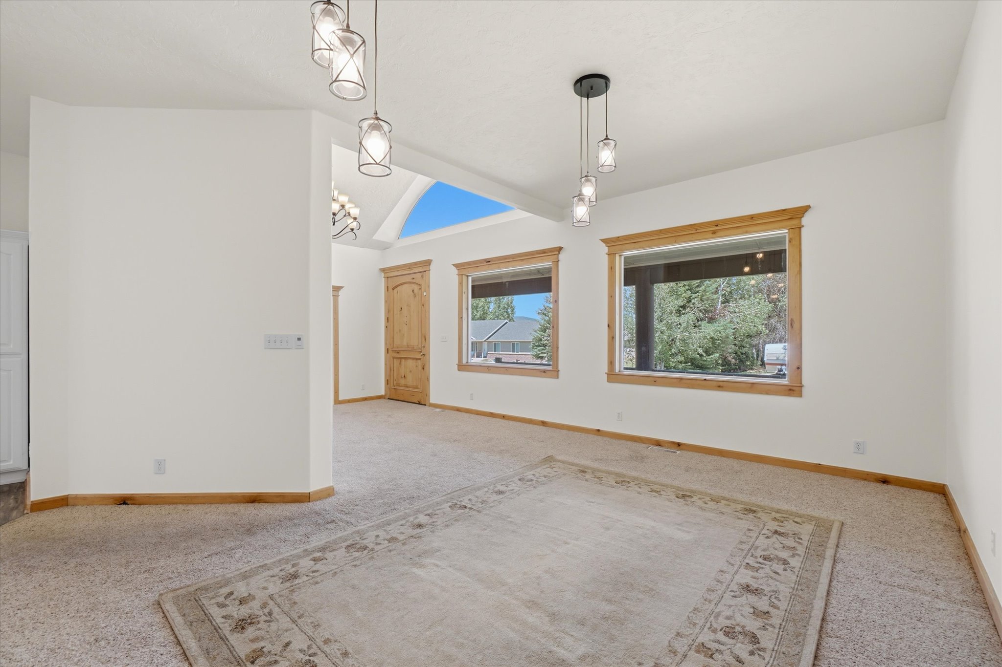 Expansive room featuring vaulted ceilings with a skylight, multiple windows with wood trim, and contemporary pendant lighting fixtures