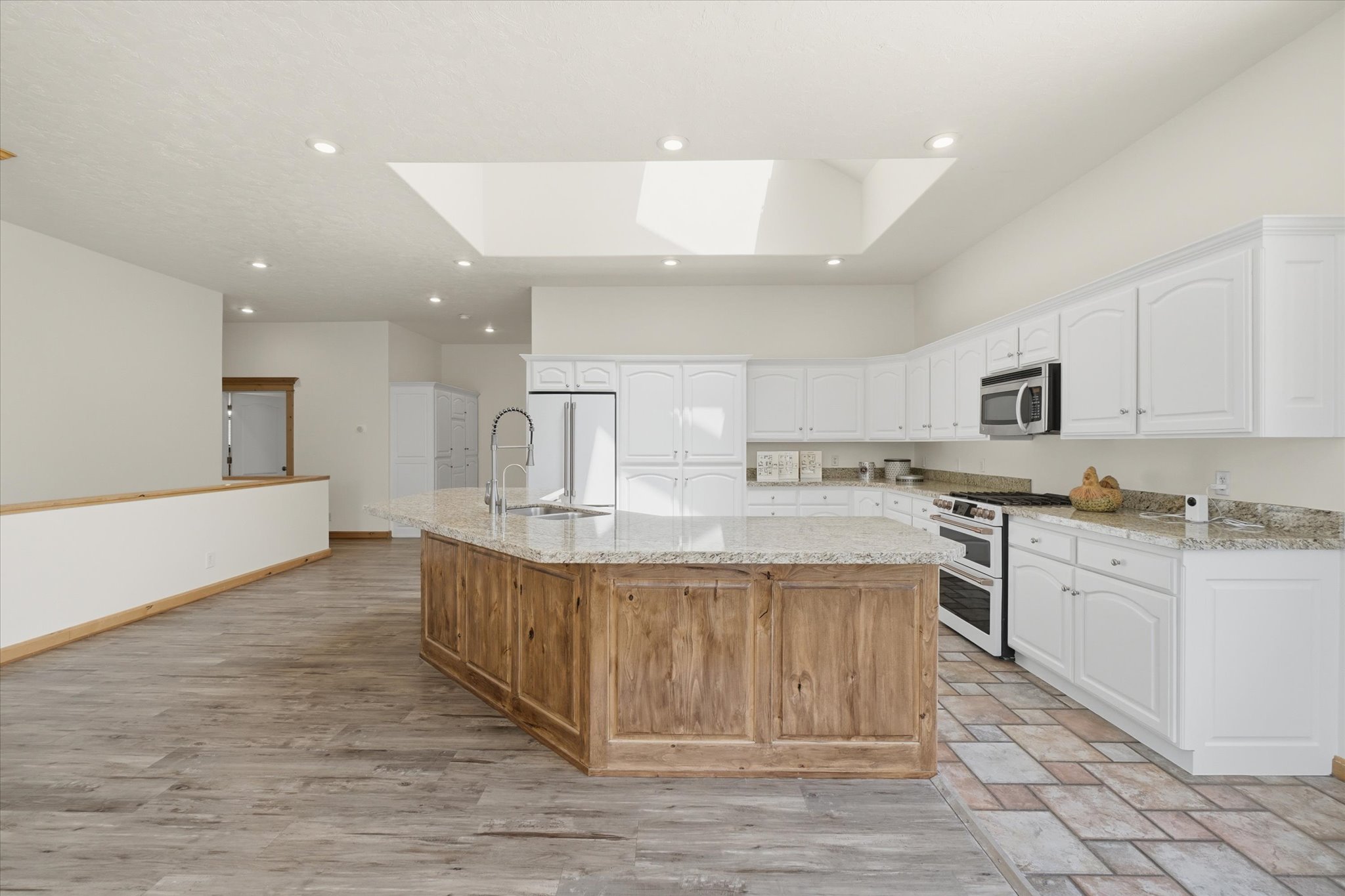 Spacious kitchen featuring a large wood-paneled island with an undermount sink, granite countertops, and extensive white cabinetry