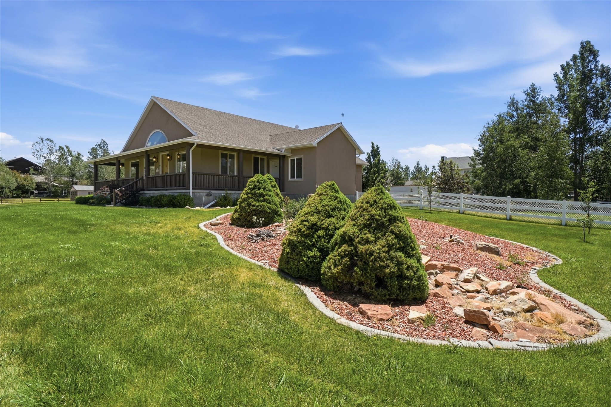 Expansive green lawn with a defined landscaping bed featuring decorative rocks and evergreen shrubs