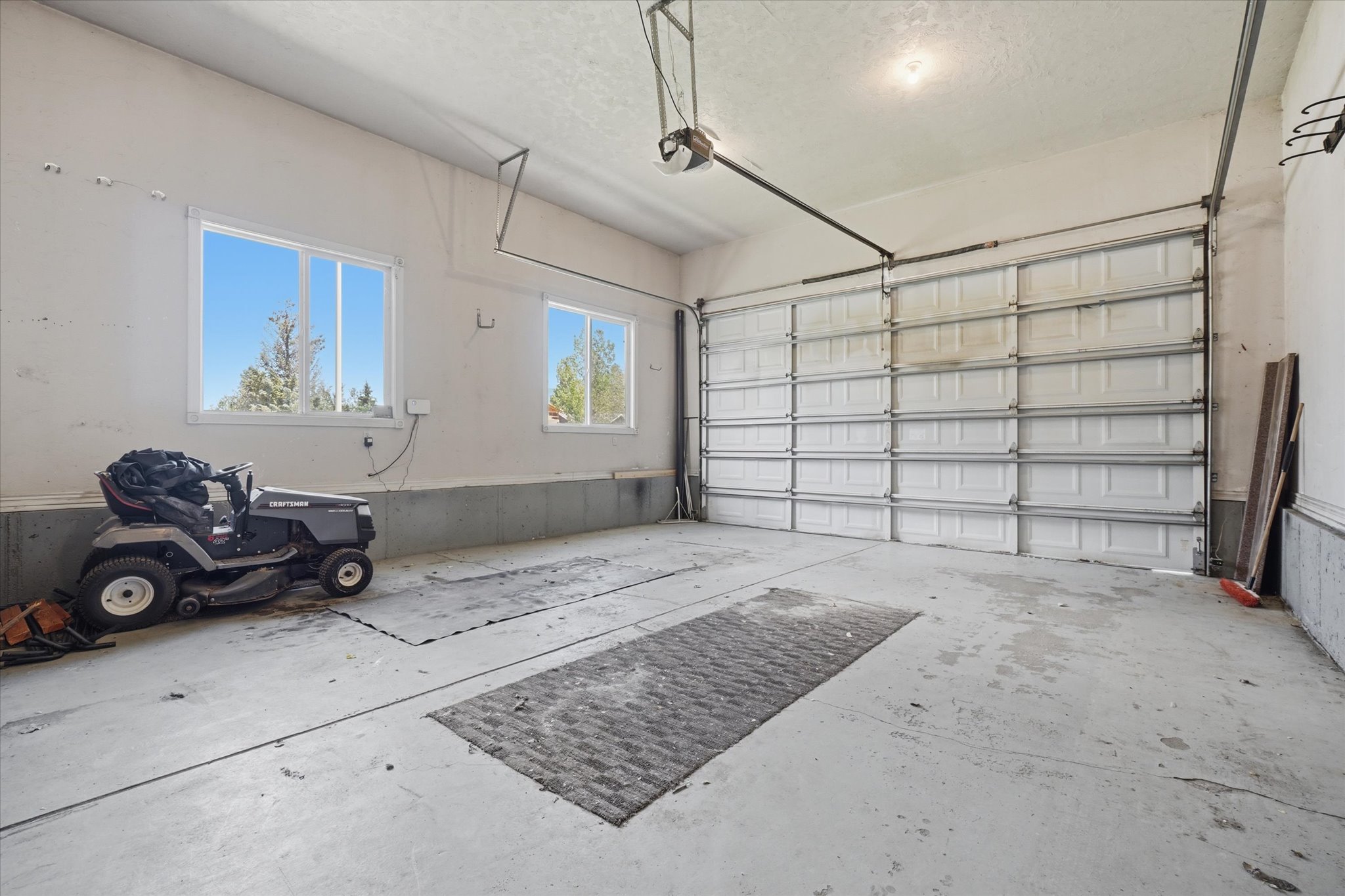 Spacious garage featuring a large automatic overhead door, concrete flooring, and two windows providing natural light