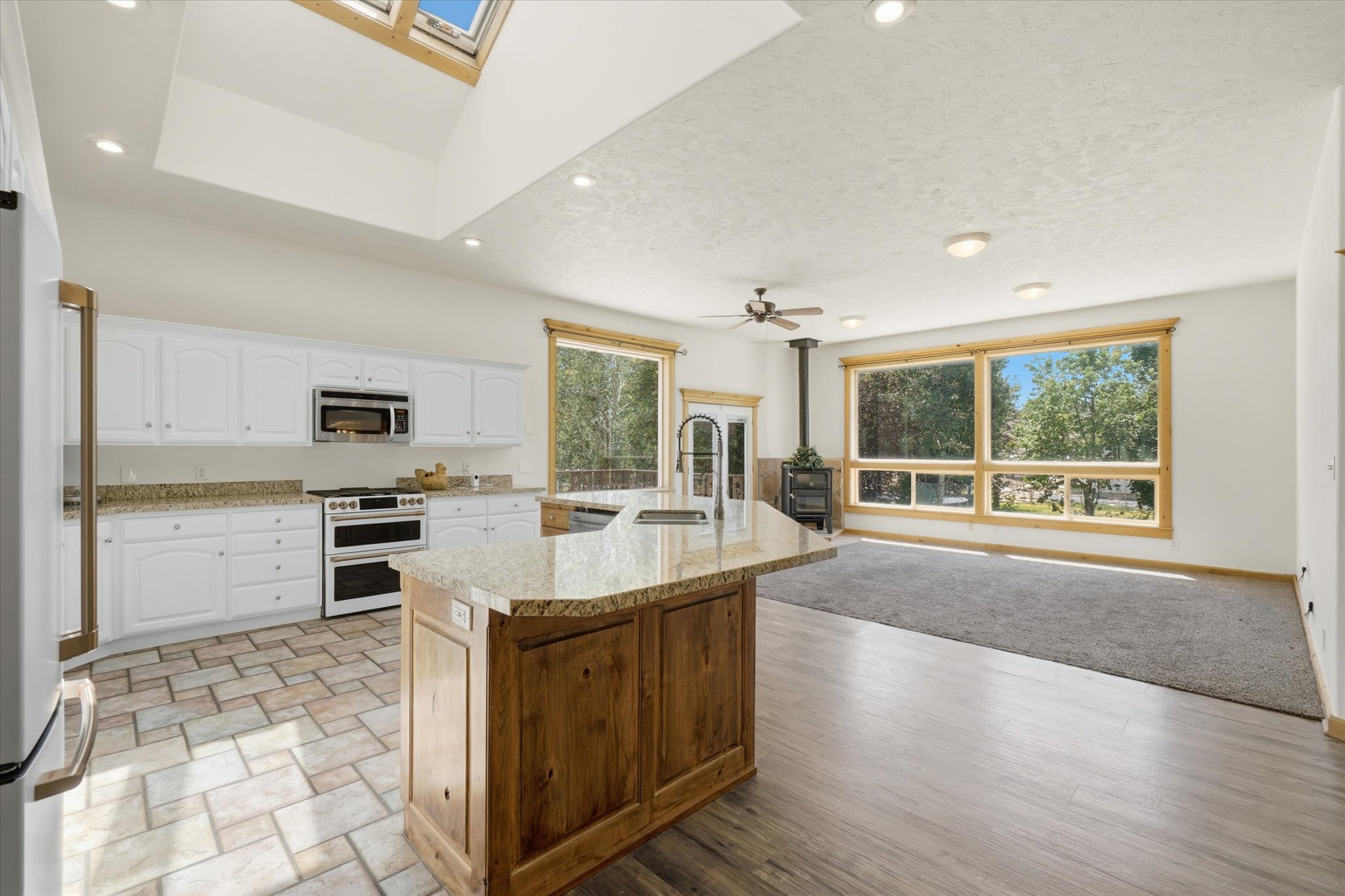 Open-concept kitchen and living area featuring a large center island with a granite countertop, white cabinetry, stainless steel appliances, and a skylight