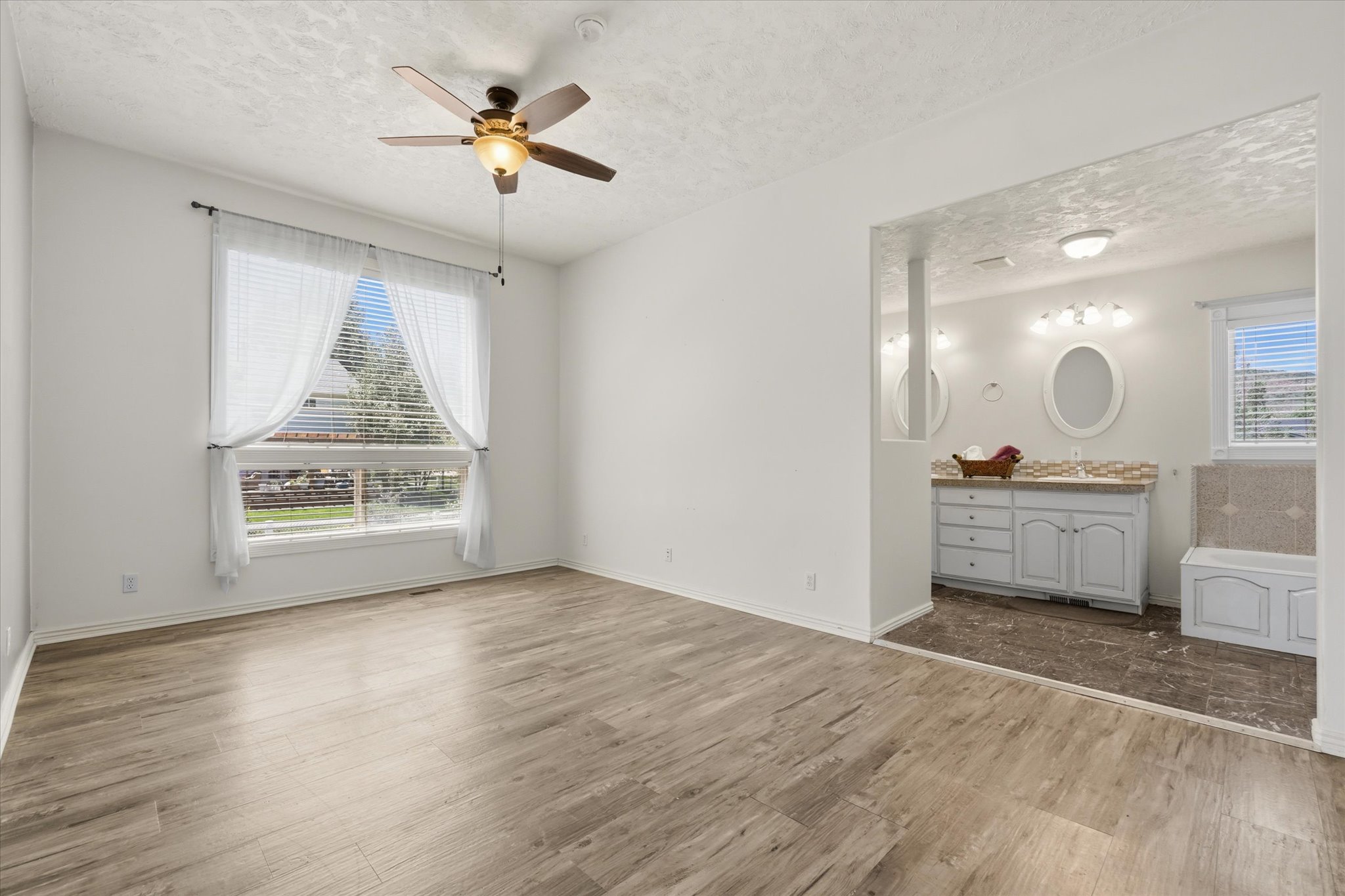 Spacious room featuring wood-finish flooring, a large window with blinds, and a ceiling fan with integrated lighting