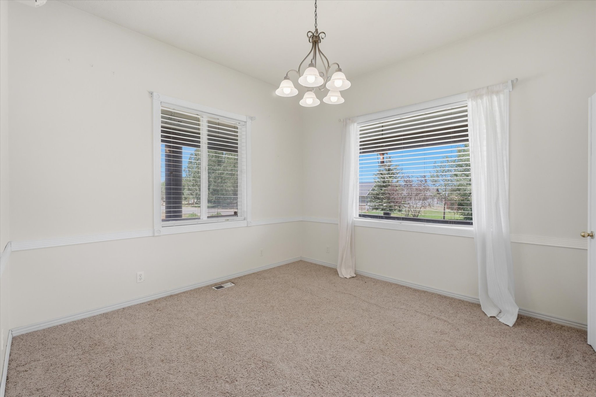 Carpeted interior space featuring dual windows with blinds, a five-light chandelier, and wainscoting