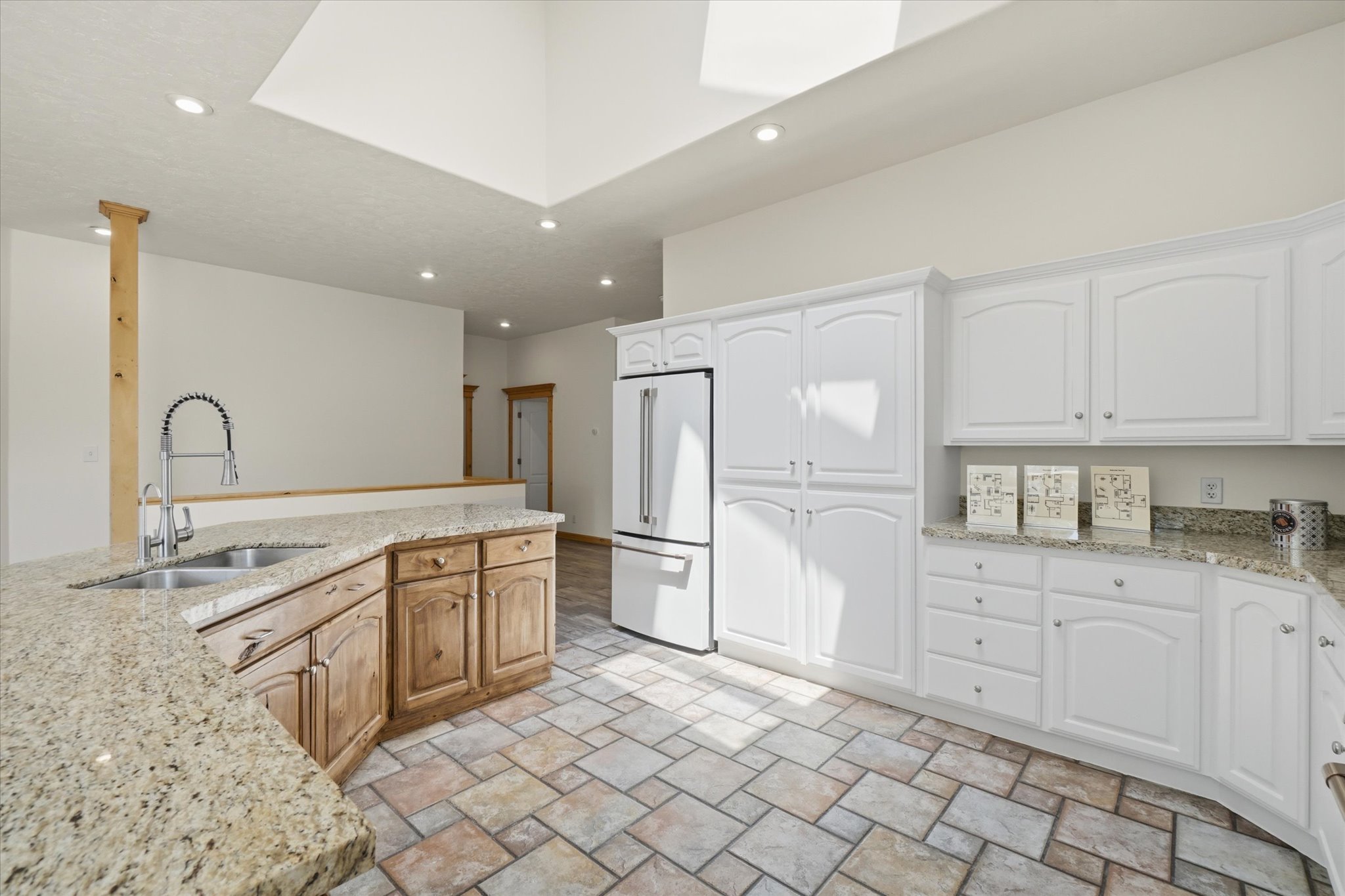 Spacious kitchen featuring white cabinetry, light granite countertops, a double basin sink with a high-arc faucet, integrated appliances, and varied-tone tile flooring