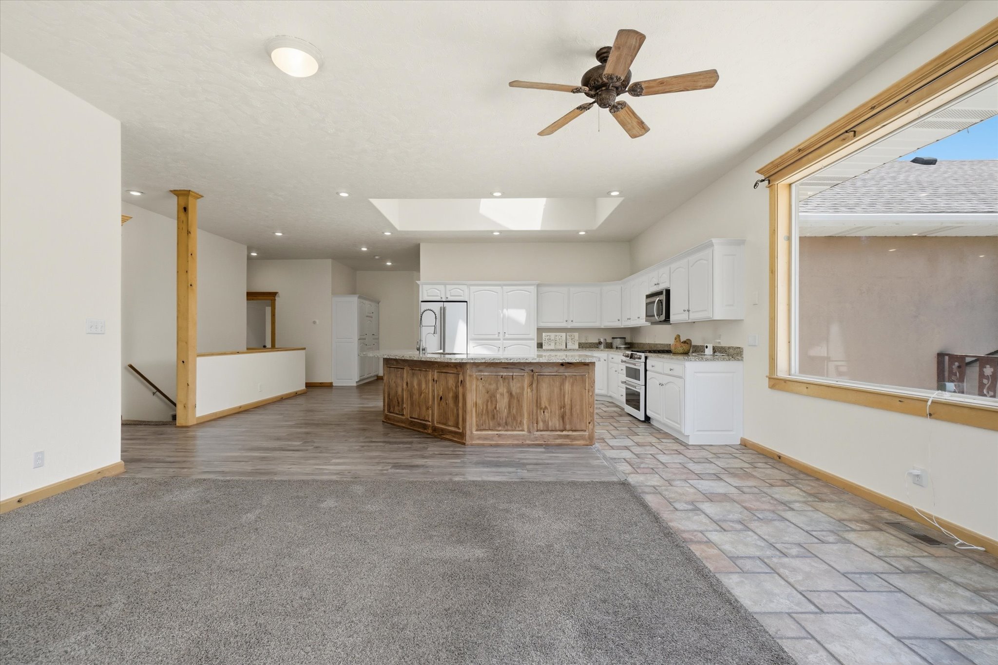 Open-concept main living area with a chef's kitchen featuring white cabinetry, stainless steel appliances, and a central wood-paneled island