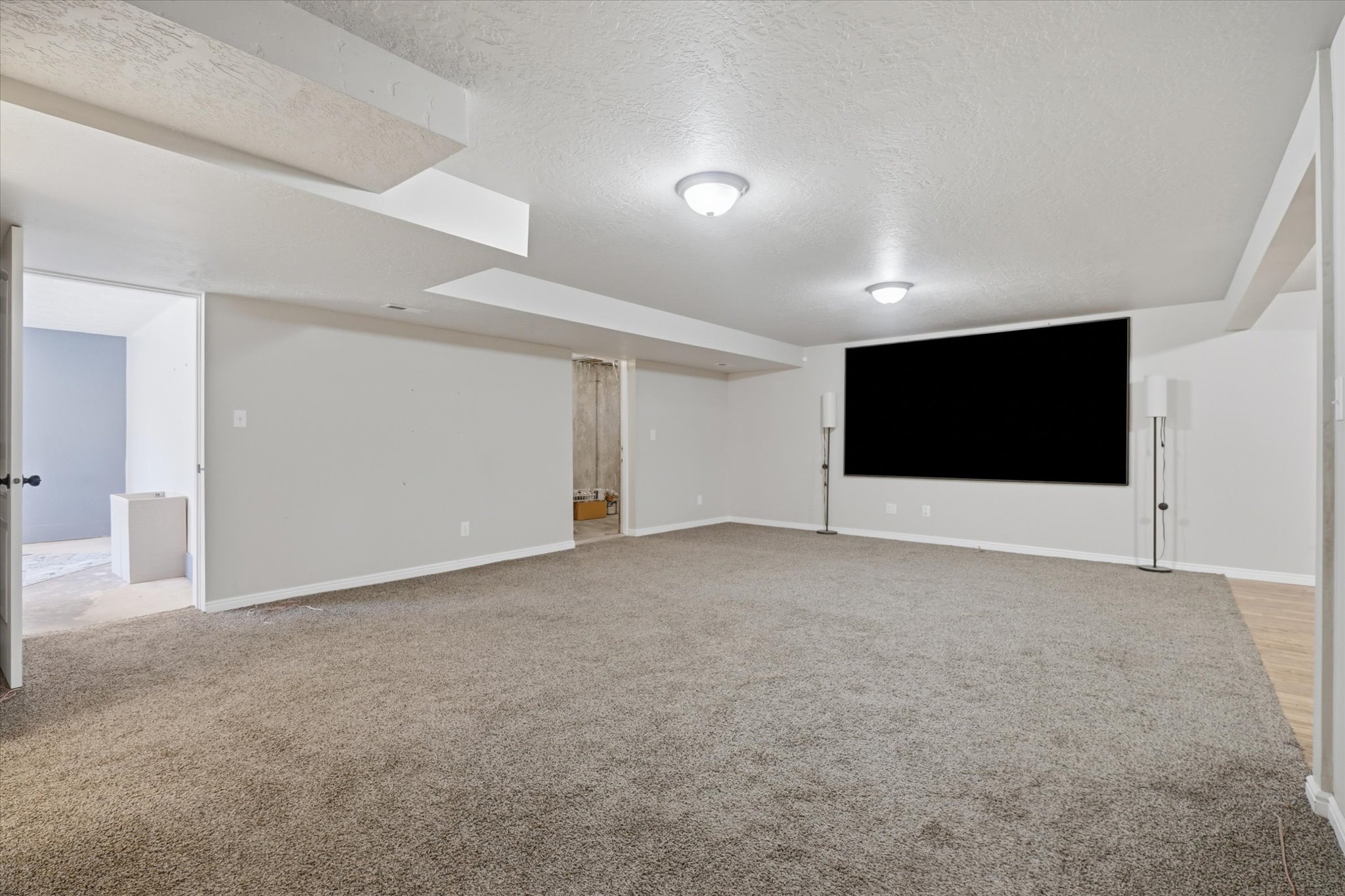 Spacious entertainment room featuring plush carpet flooring, recessed ceiling lighting, and a large wall-mounted screen
