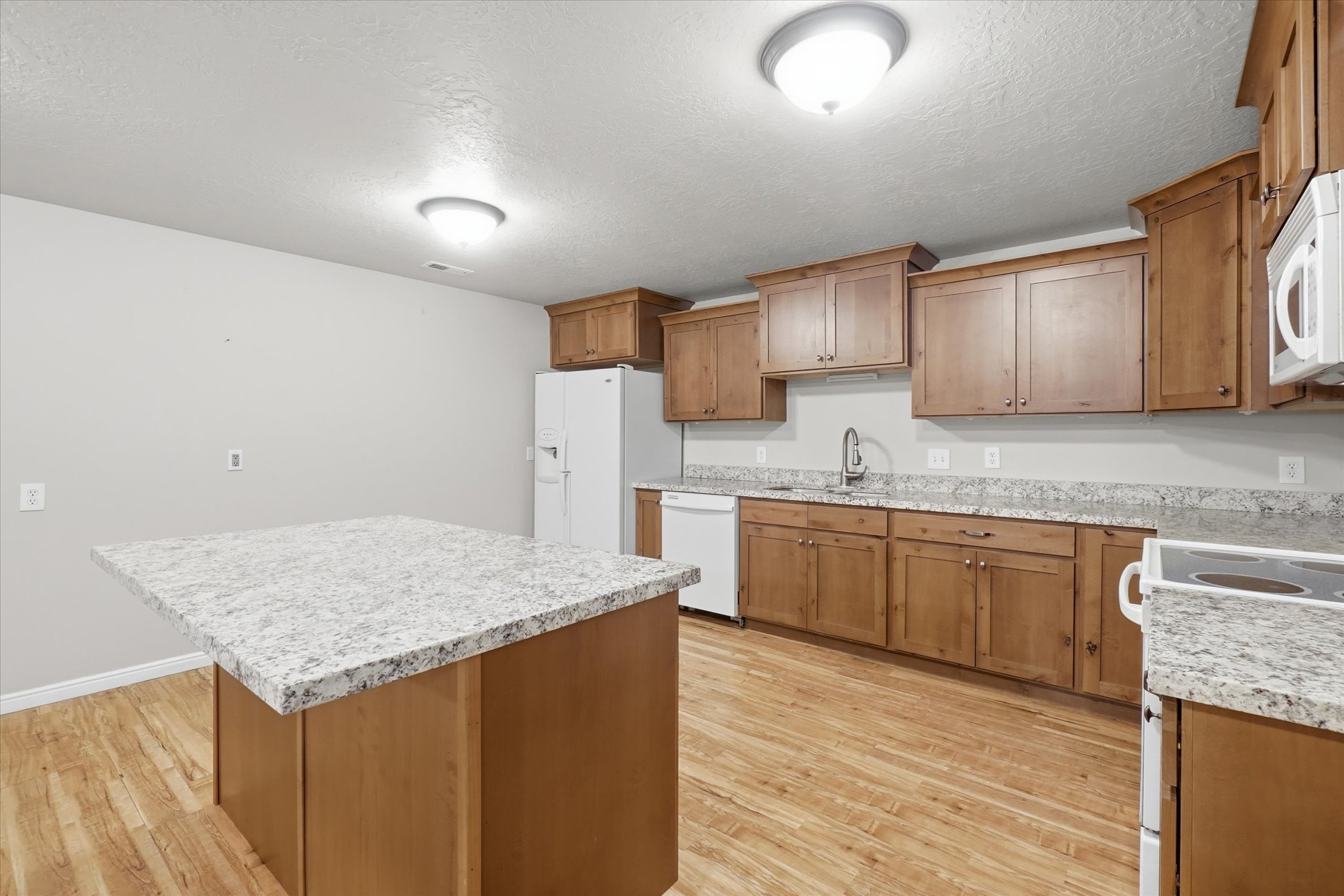 Kitchen featuring a central island, wood-finish flooring, wood cabinetry, light-toned countertops, and ceiling-mounted lighting fixtures