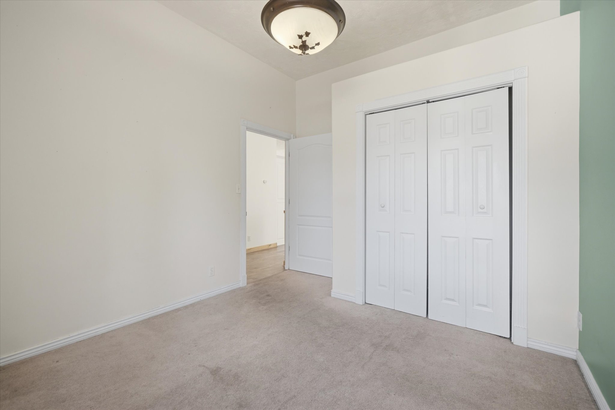 Room featuring light neutral wall paint, a ceiling-mounted light fixture, carpeted flooring, and a closet with bifold doors