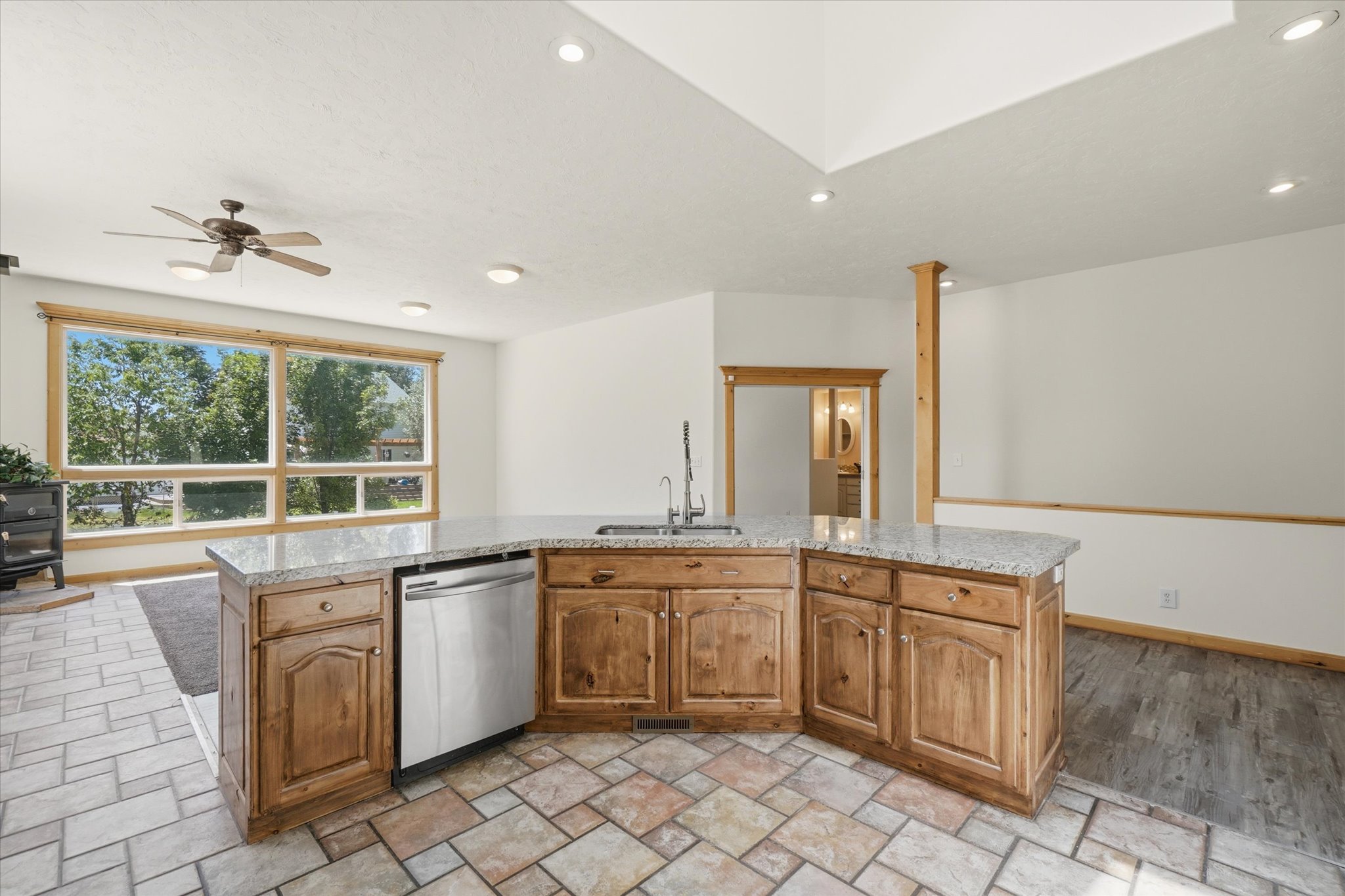 Kitchen island featuring a granite-style countertop, integrated stainless steel dishwasher, and wood cabinetry