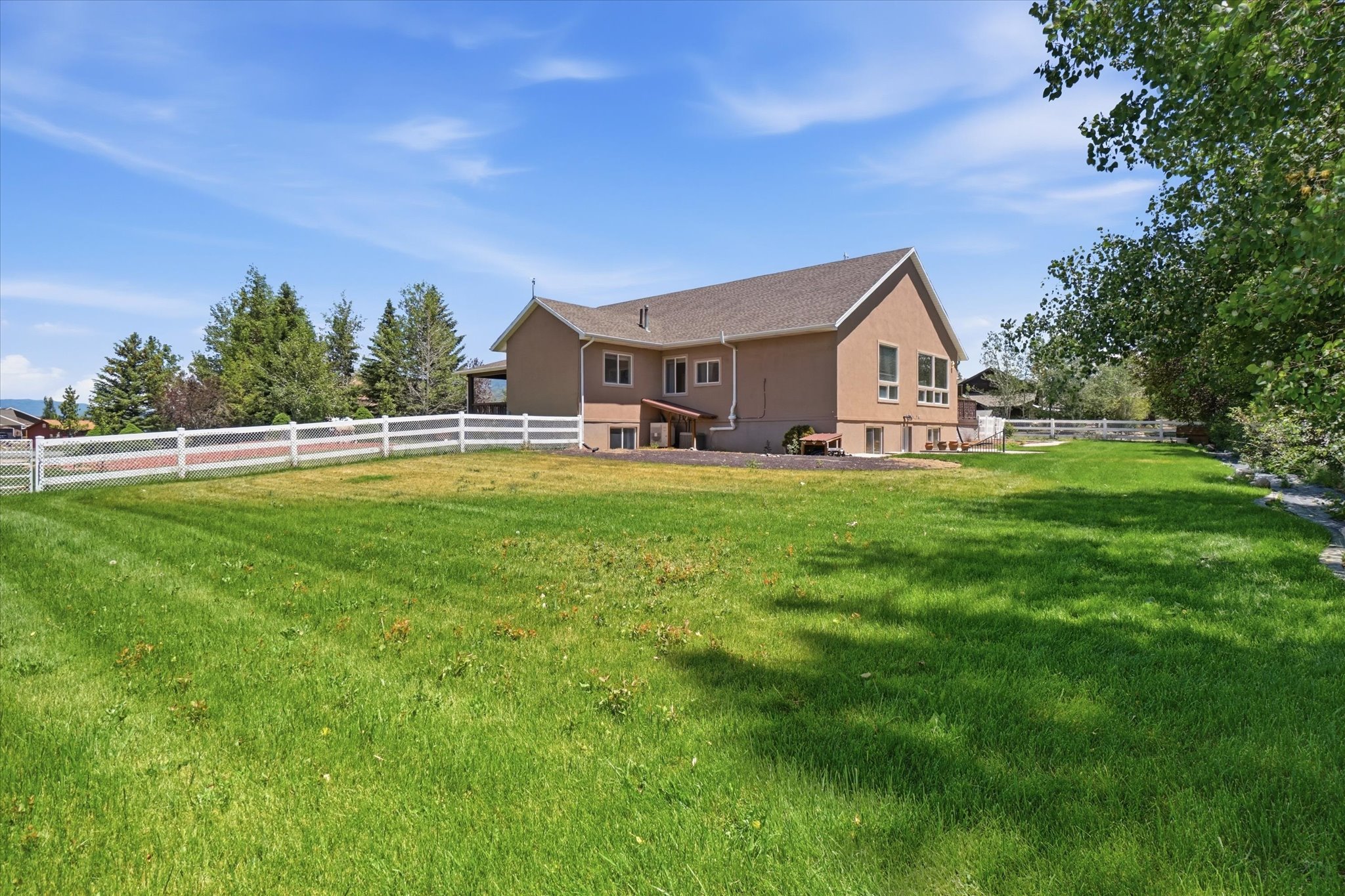 Spacious property featuring a large green lawn, white perimeter fencing, and mature trees