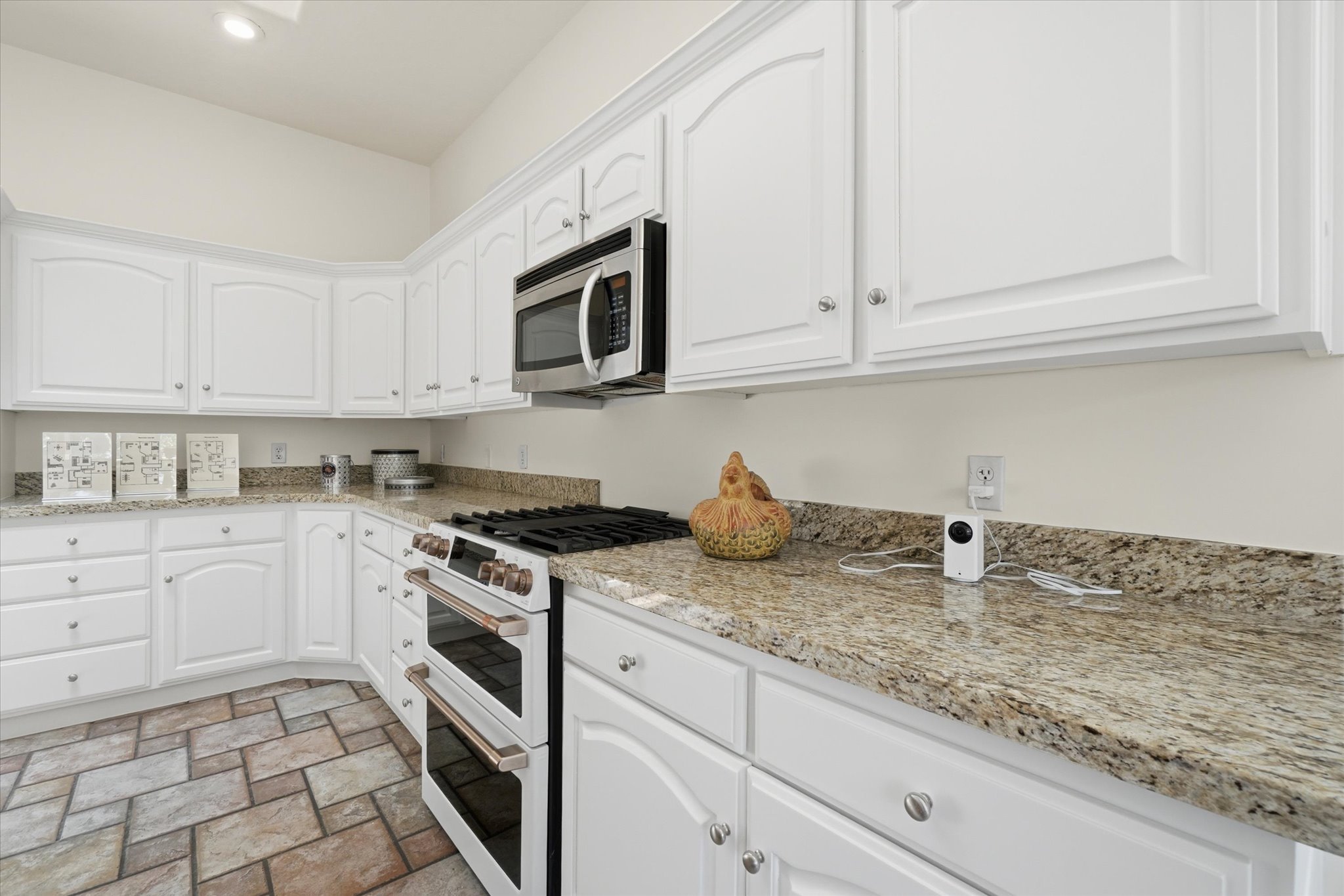Corner kitchen featuring white cabinetry, stone-finish countertops, stainless steel microwave, and a double oven range