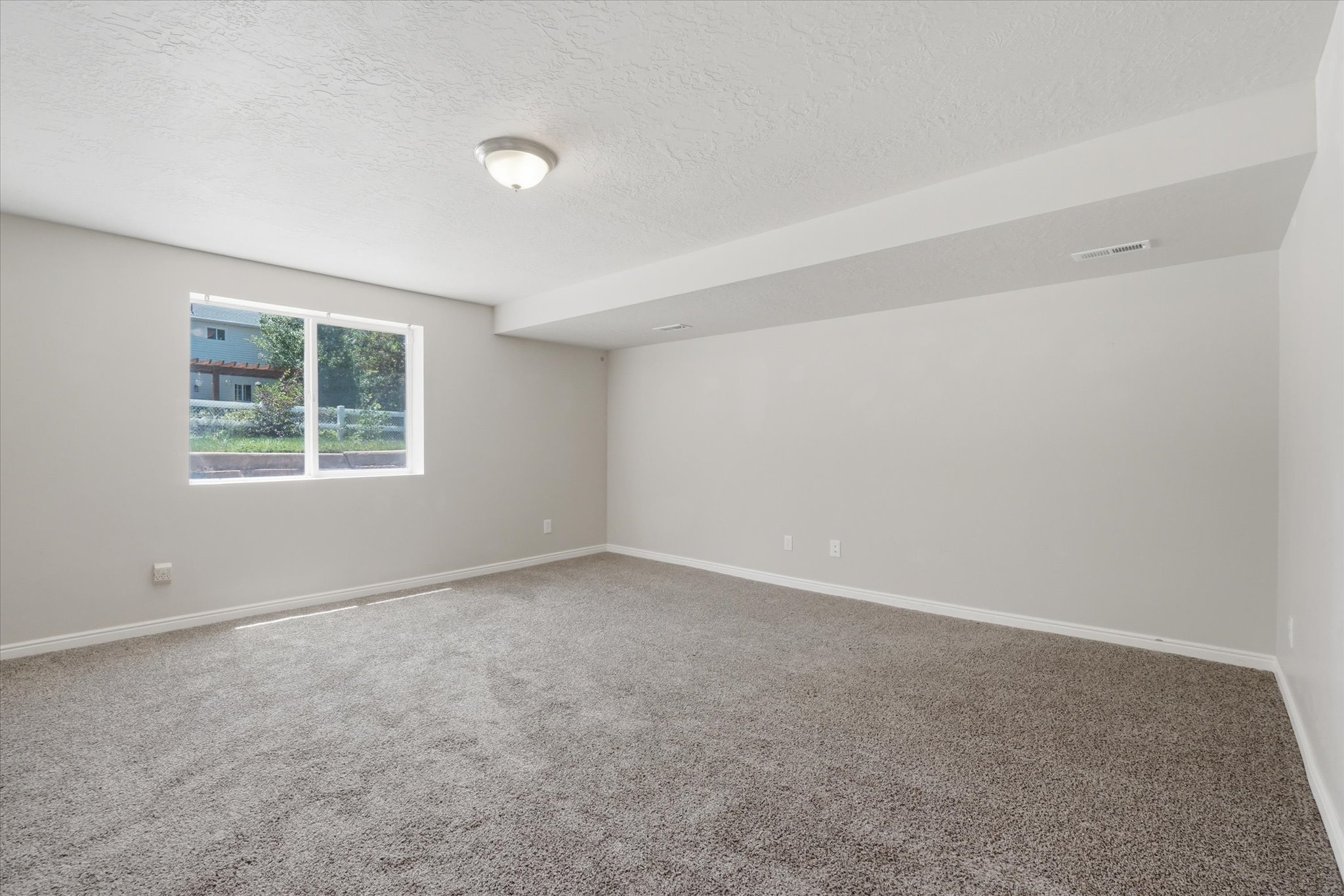 Spacious room with light gray walls, plush gray carpeting, and white baseboards