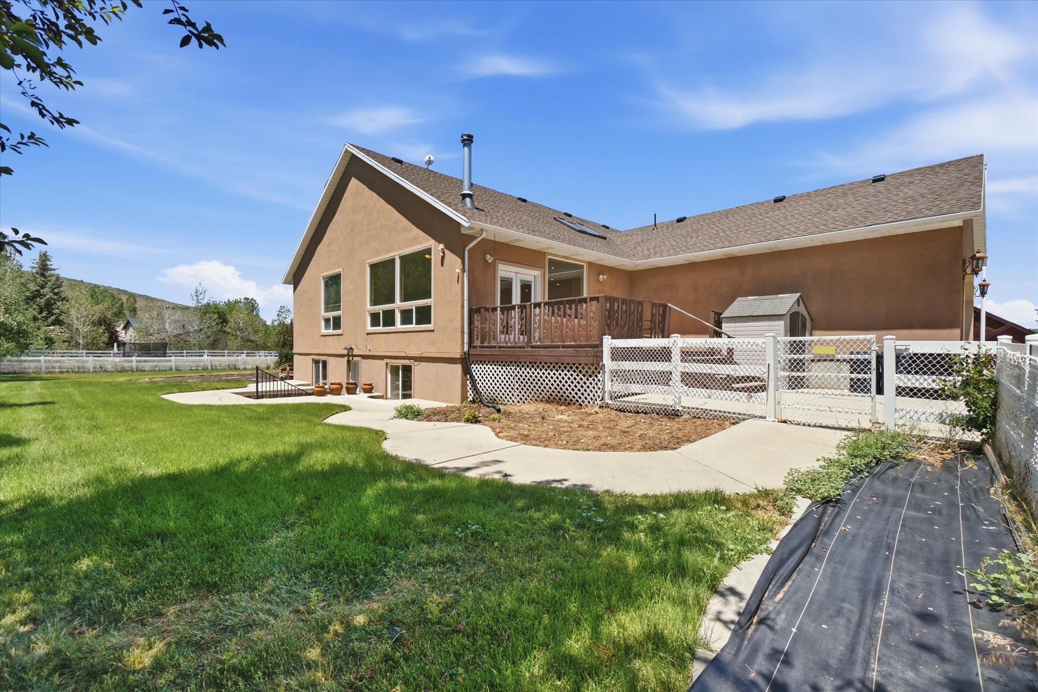 Expansive rear exterior featuring a stucco finish, multi-level deck, concrete patio, and a fenced area