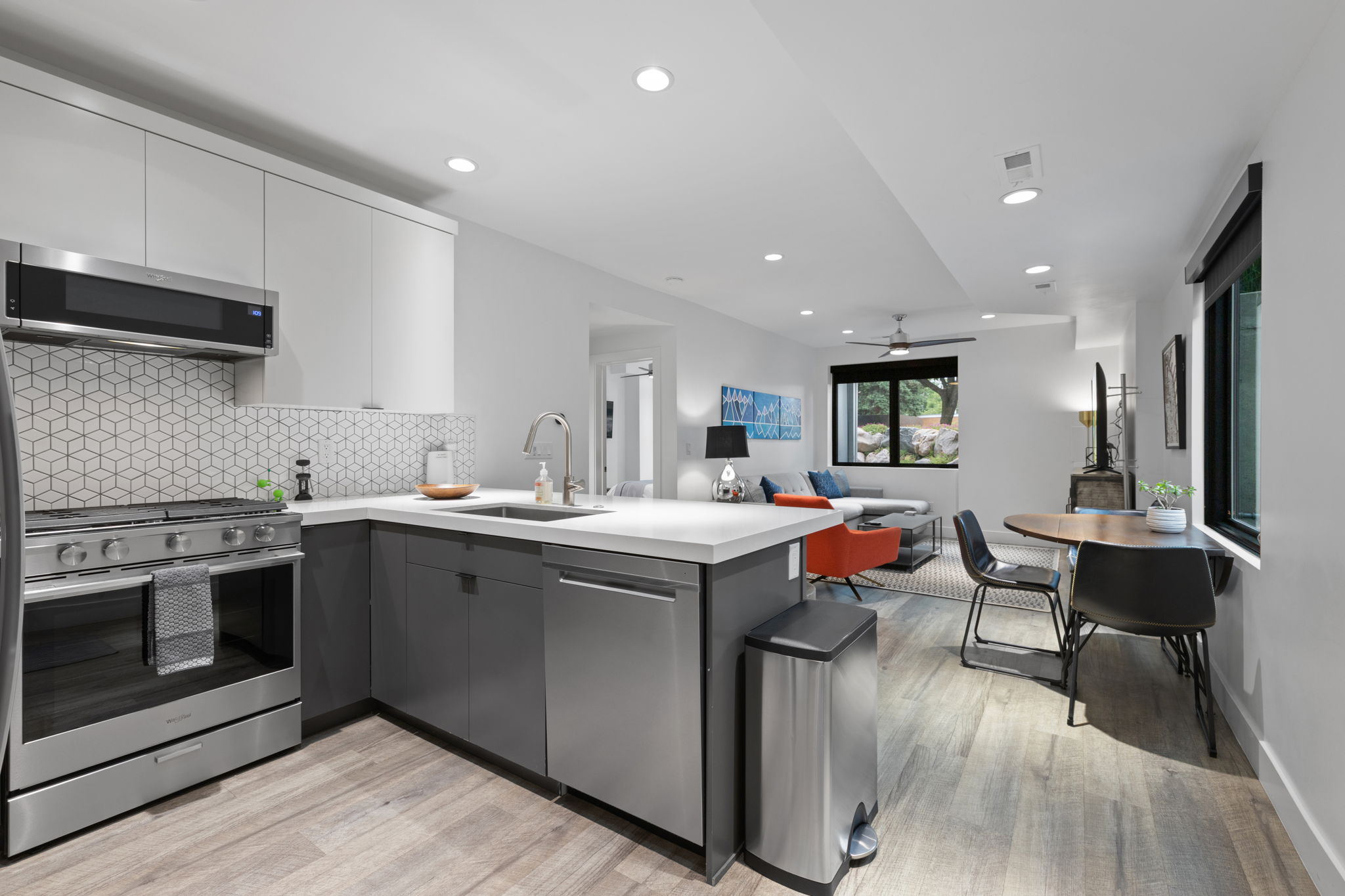 Open-concept living space with a modern kitchen featuring stainless steel appliances, a geometric tile backsplash, and light wood-finish flooring