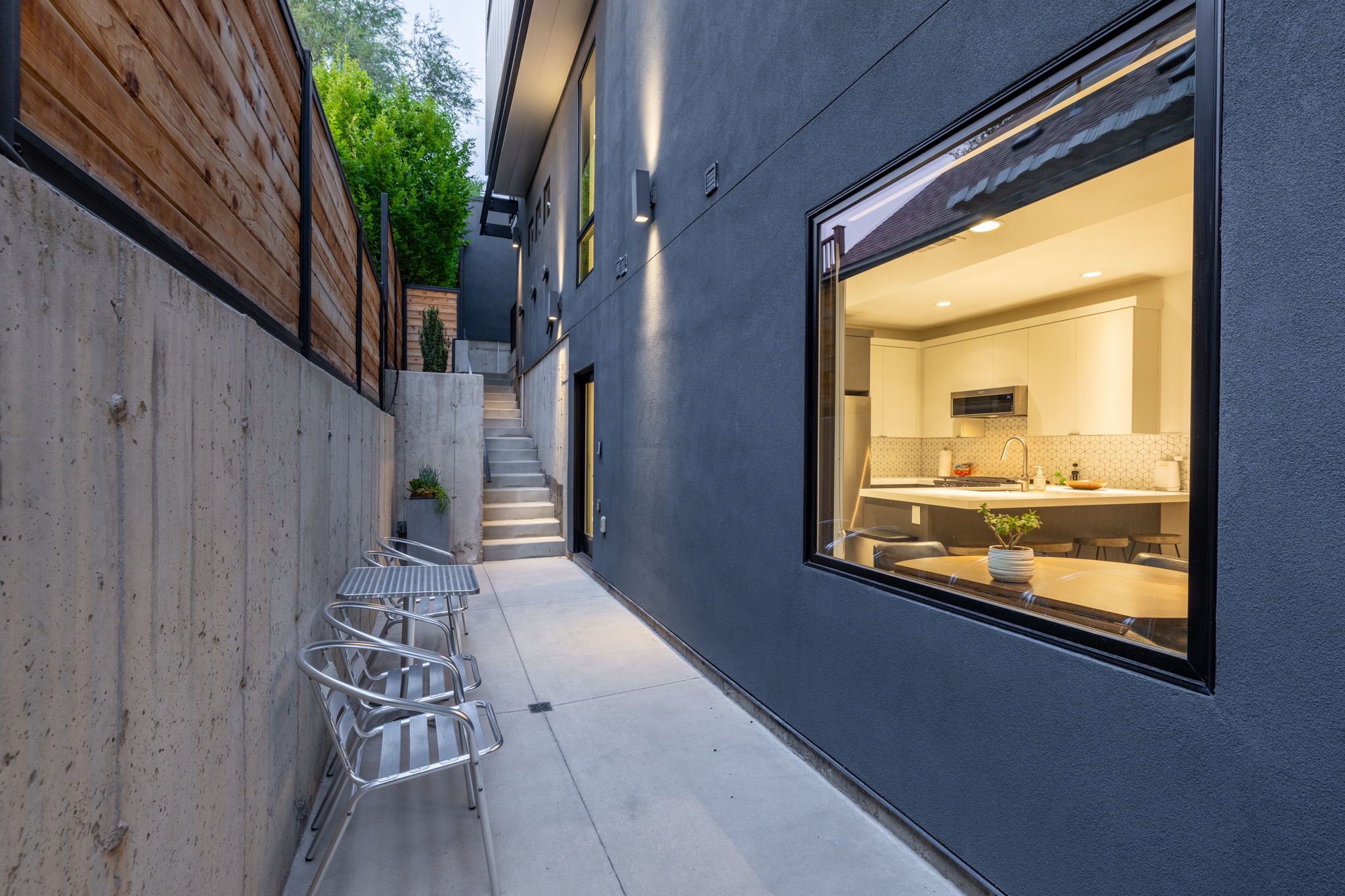 Modern exterior featuring a prominent window revealing a kitchen with white cabinetry and a patterned backsplash